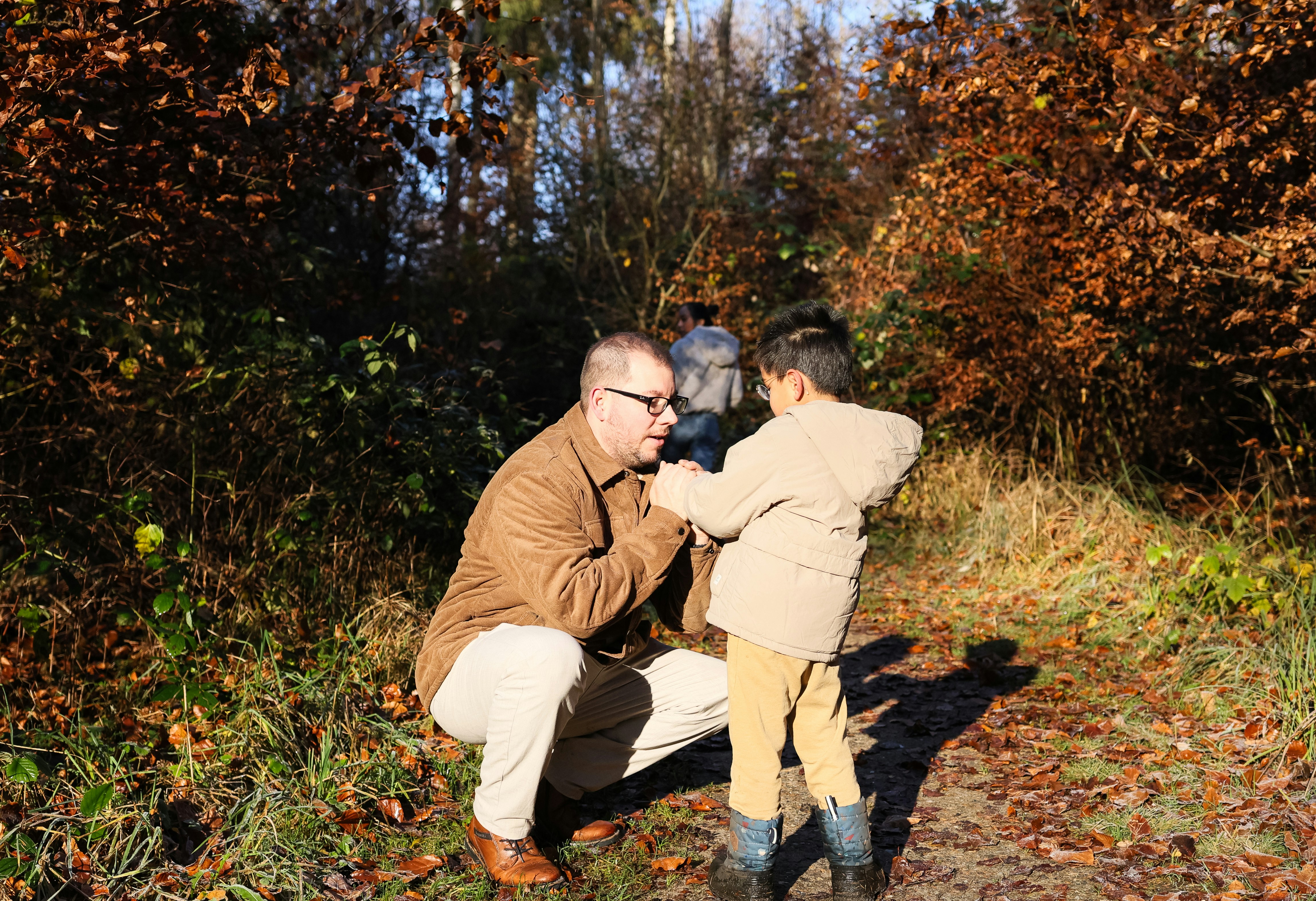 Father and son interact in autumn forest path.