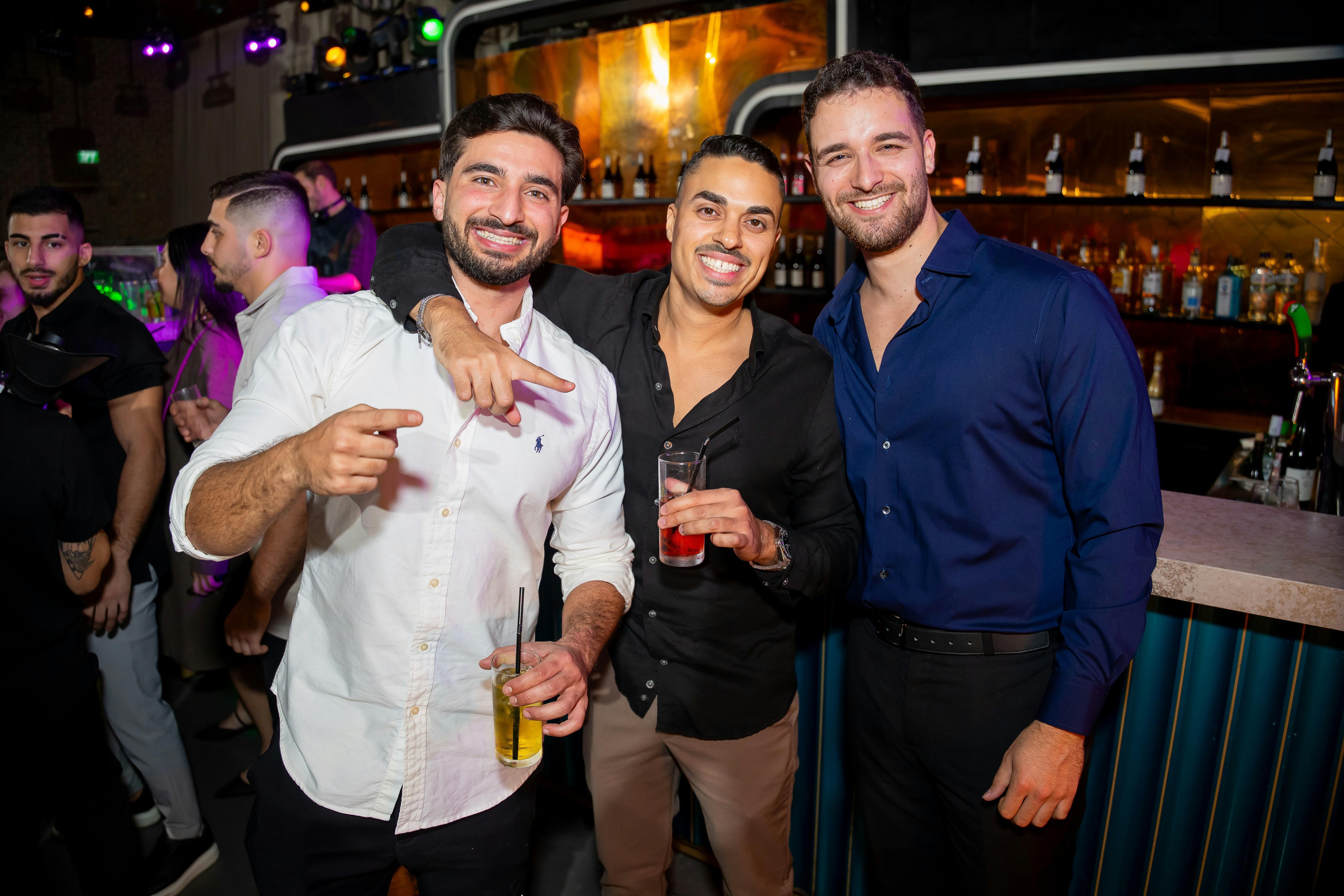 Three smiling men holding drinks in a nightclub.