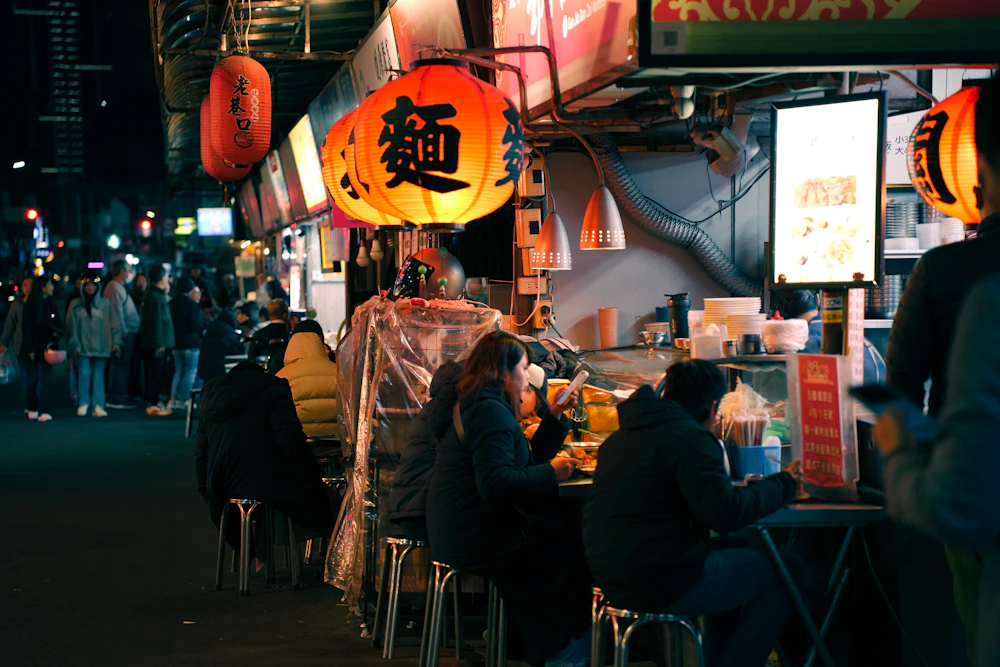 Diners seated at a noodle stall under red paper lanterns