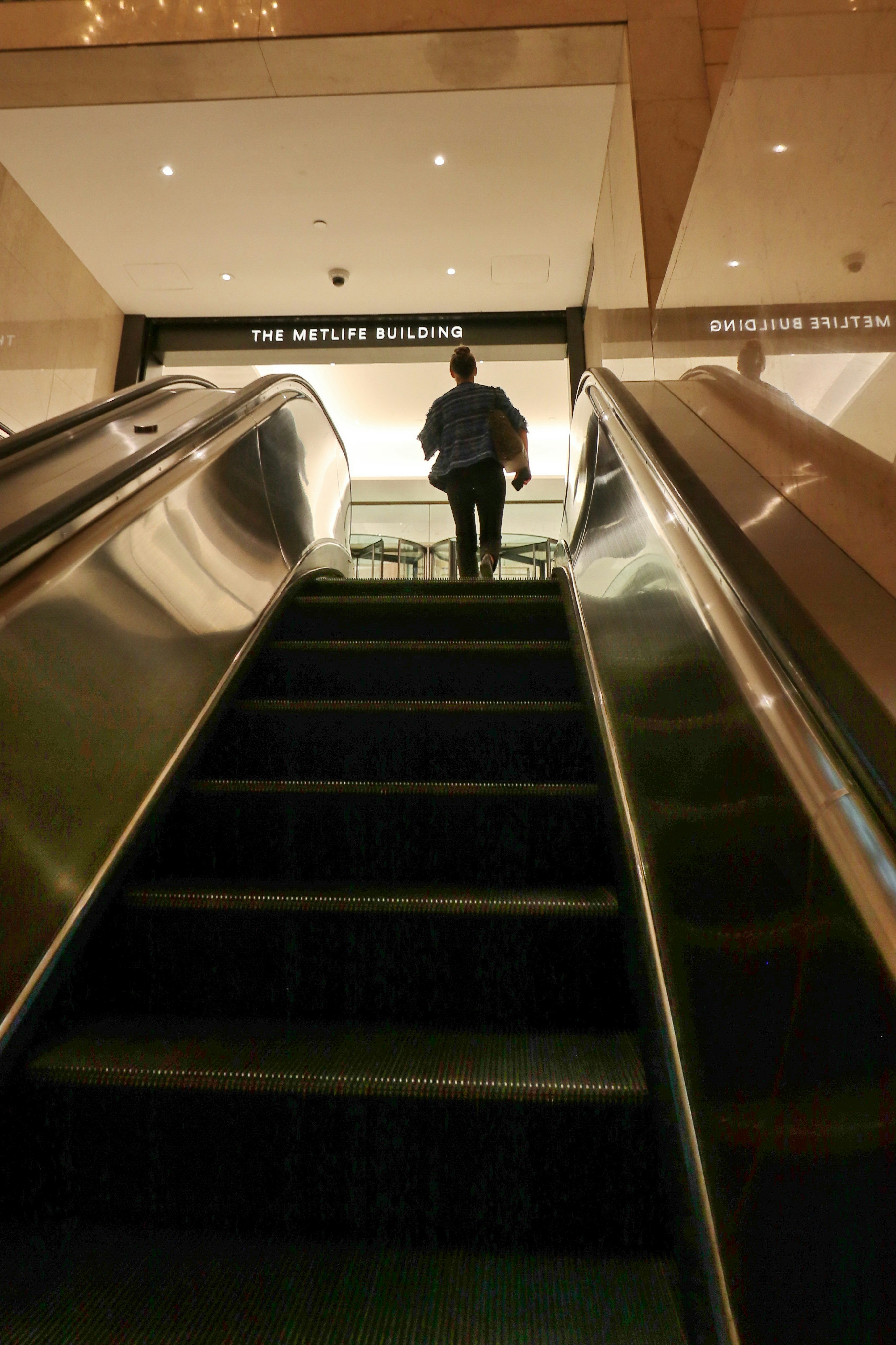 Person ascends escalator towards the metlife building entrance.