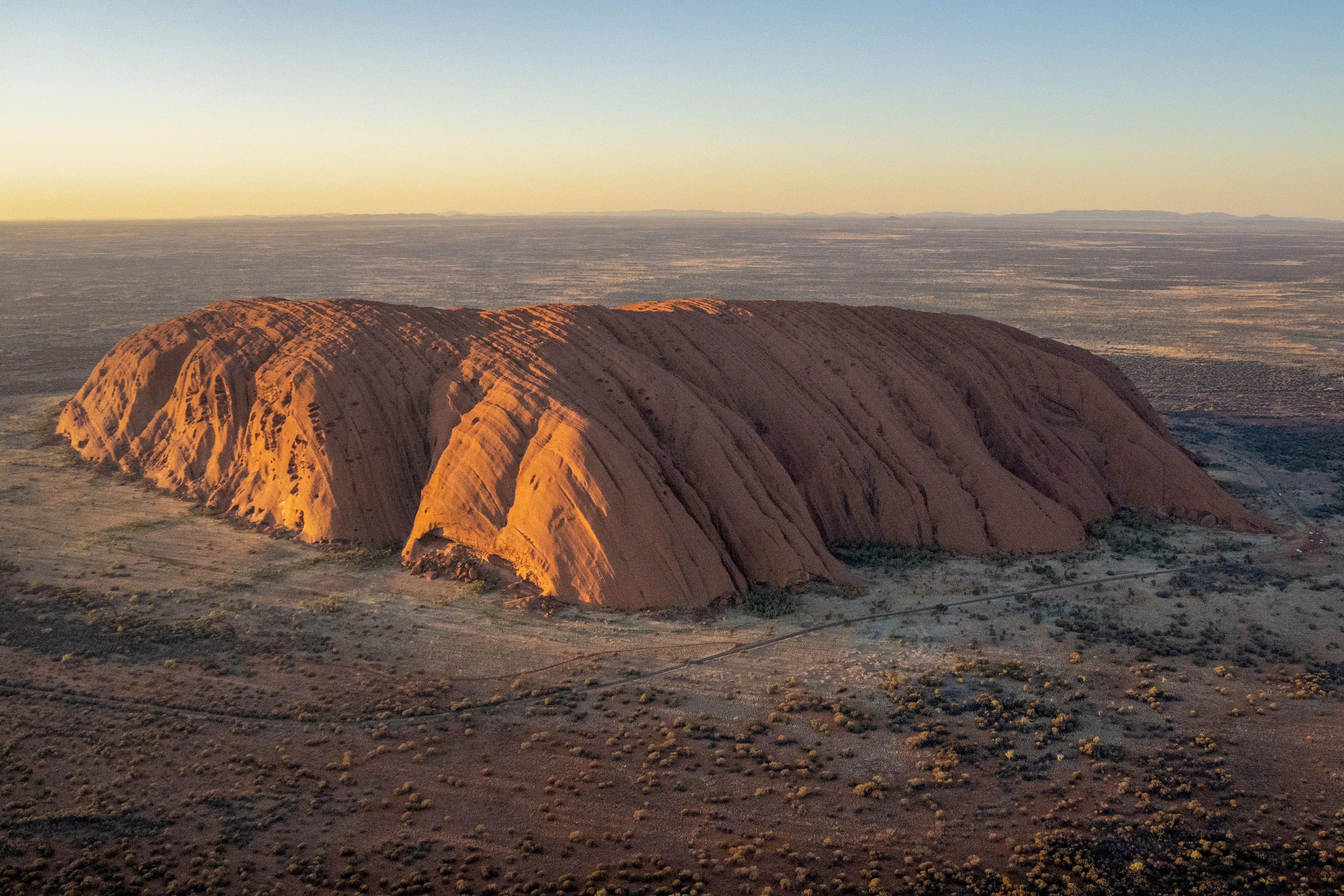 Uluru auksinėje ankstyvo ryto šviesoje, žvelgiant iš oro į plačią dykumą