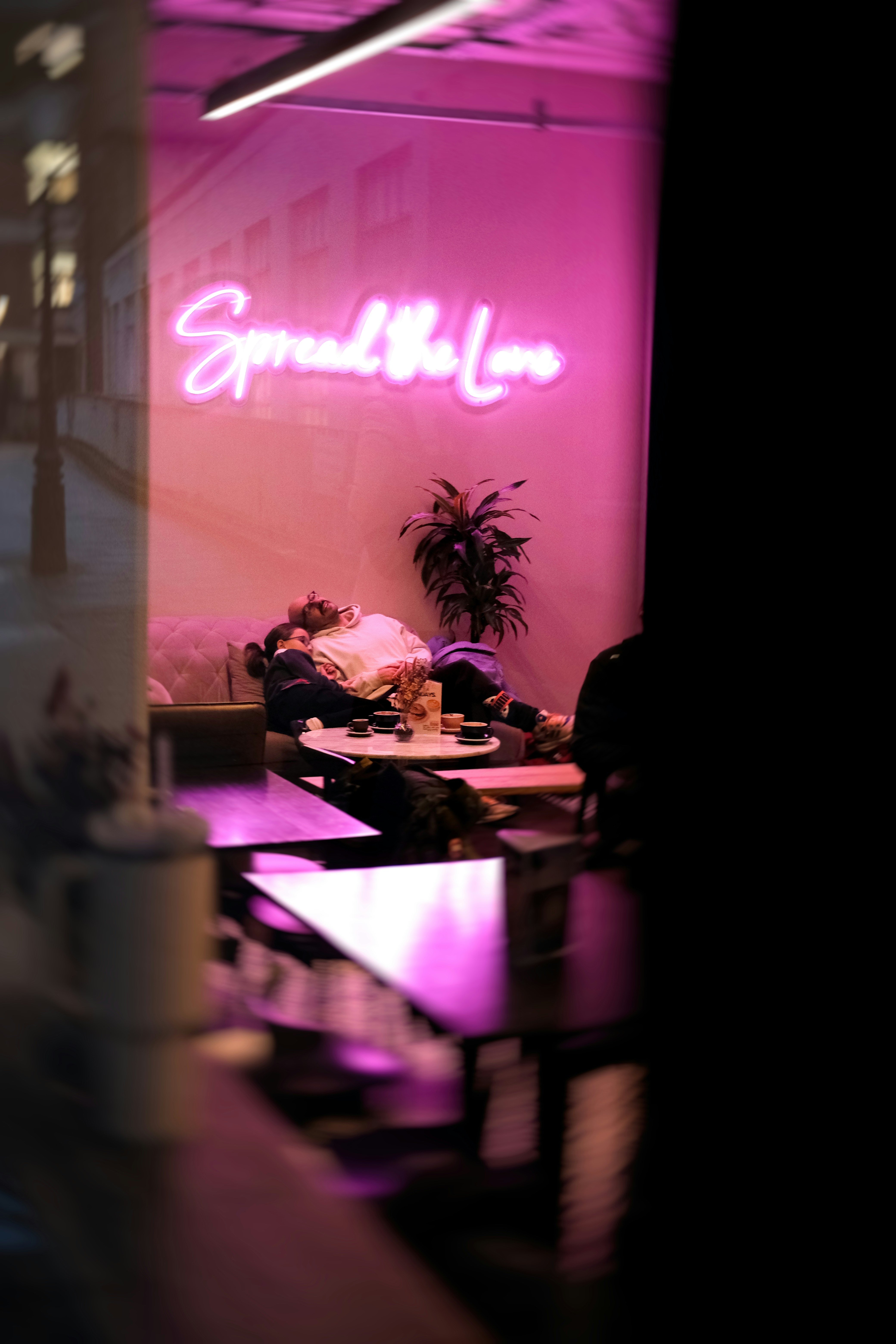Person sleeping under neon sign in cafe.
