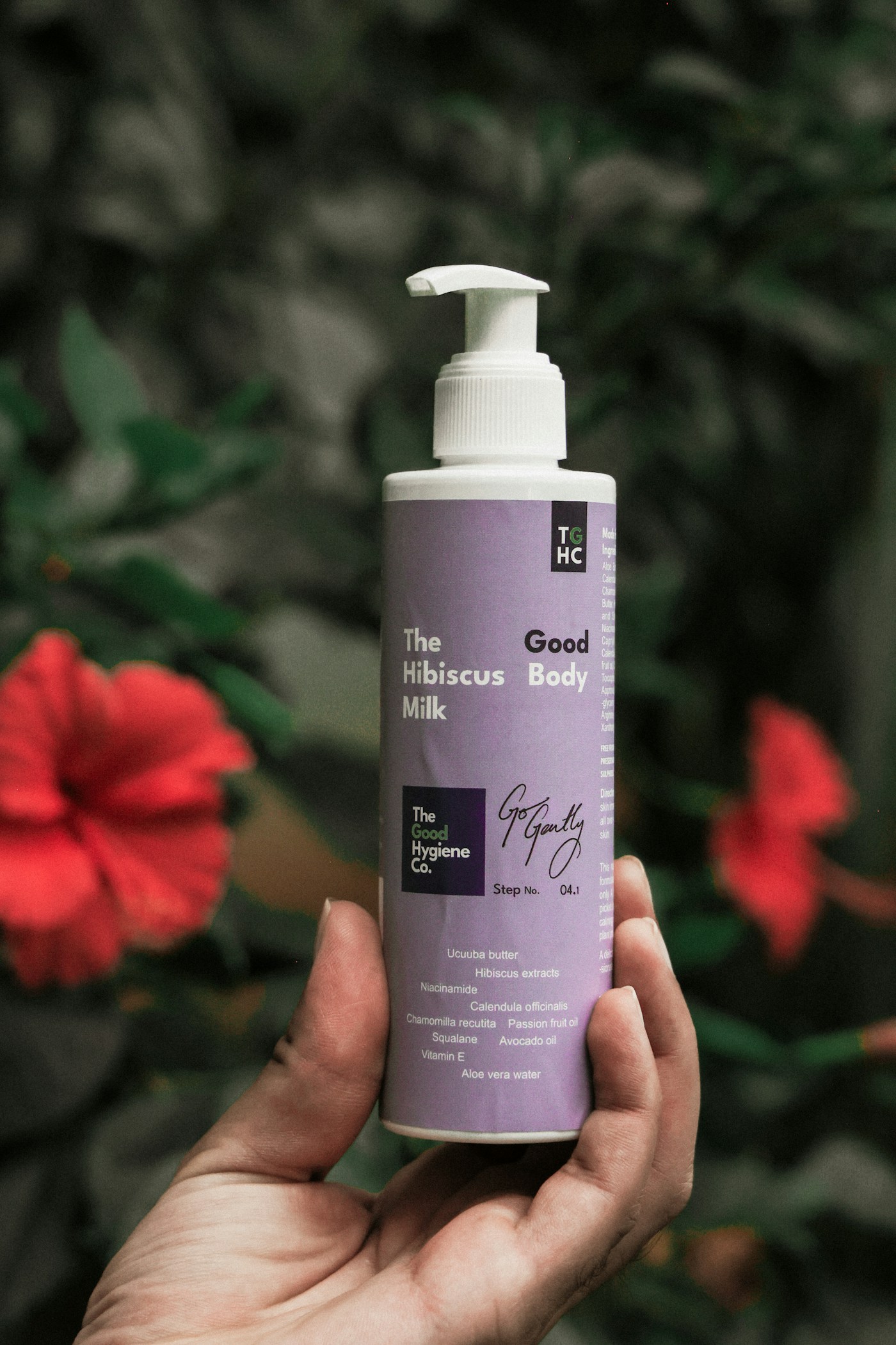 Hand holding amber lotion bottle with hibiscus