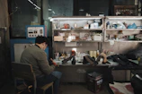 Man working at a cluttered workbench with shelves above shelves