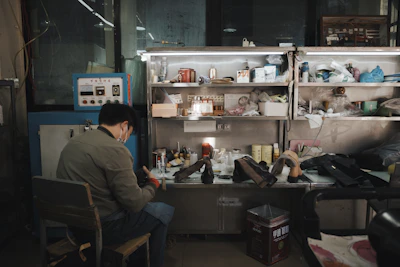 Man working at a cluttered workbench with shelves above shelves
