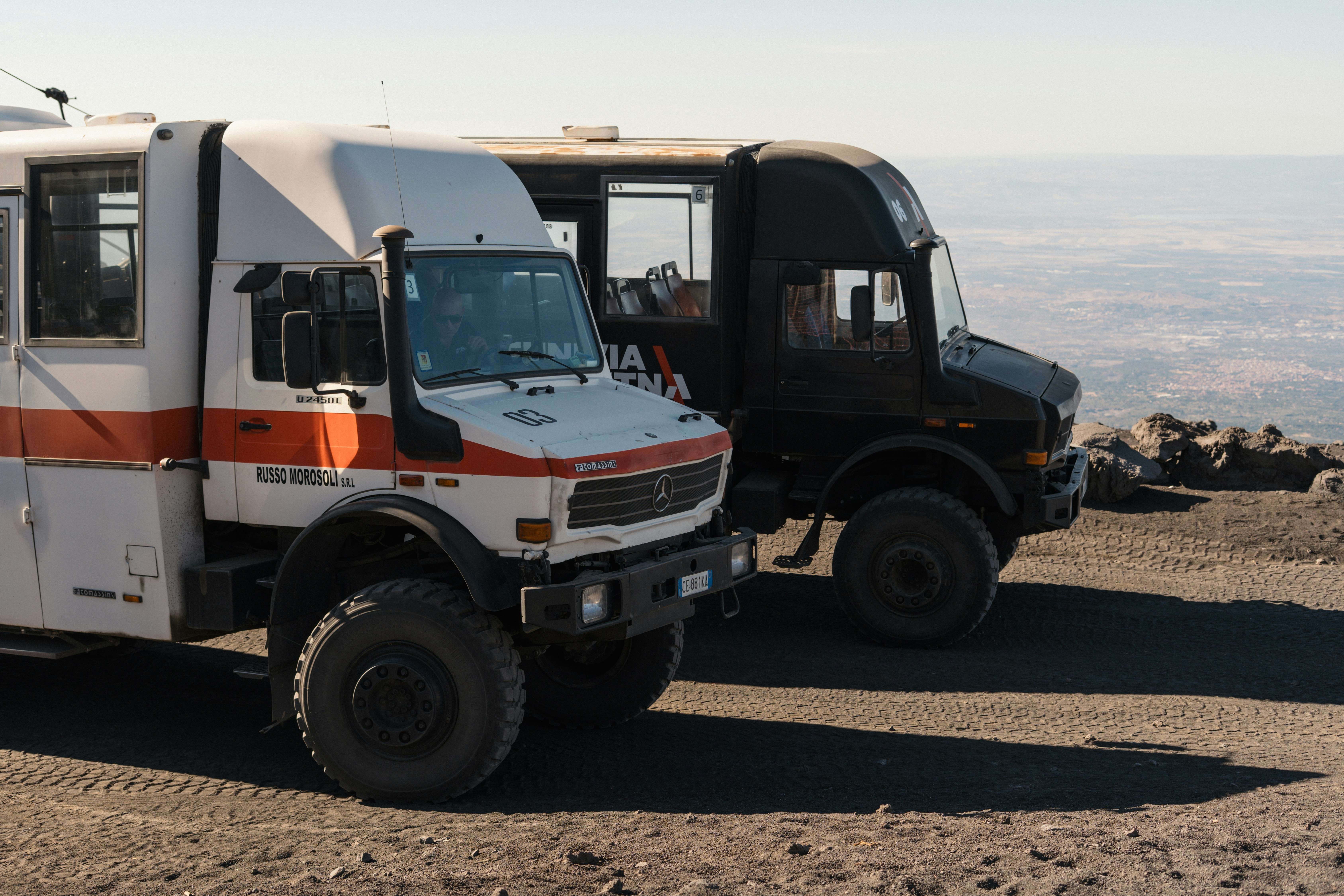 Two rugged off-road trucks parked on a dirt road.