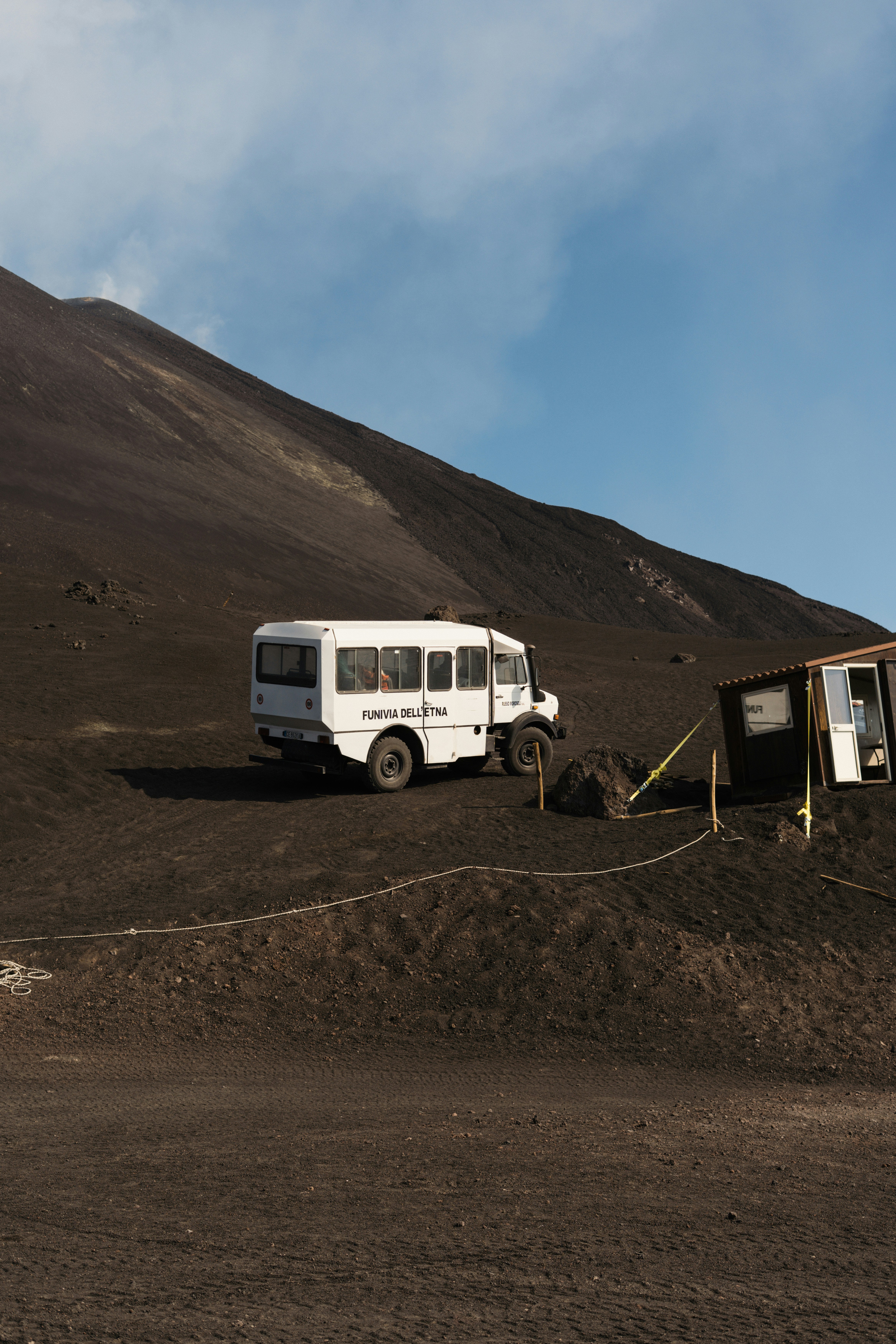 White bus parked on a dark, volcanic slope.