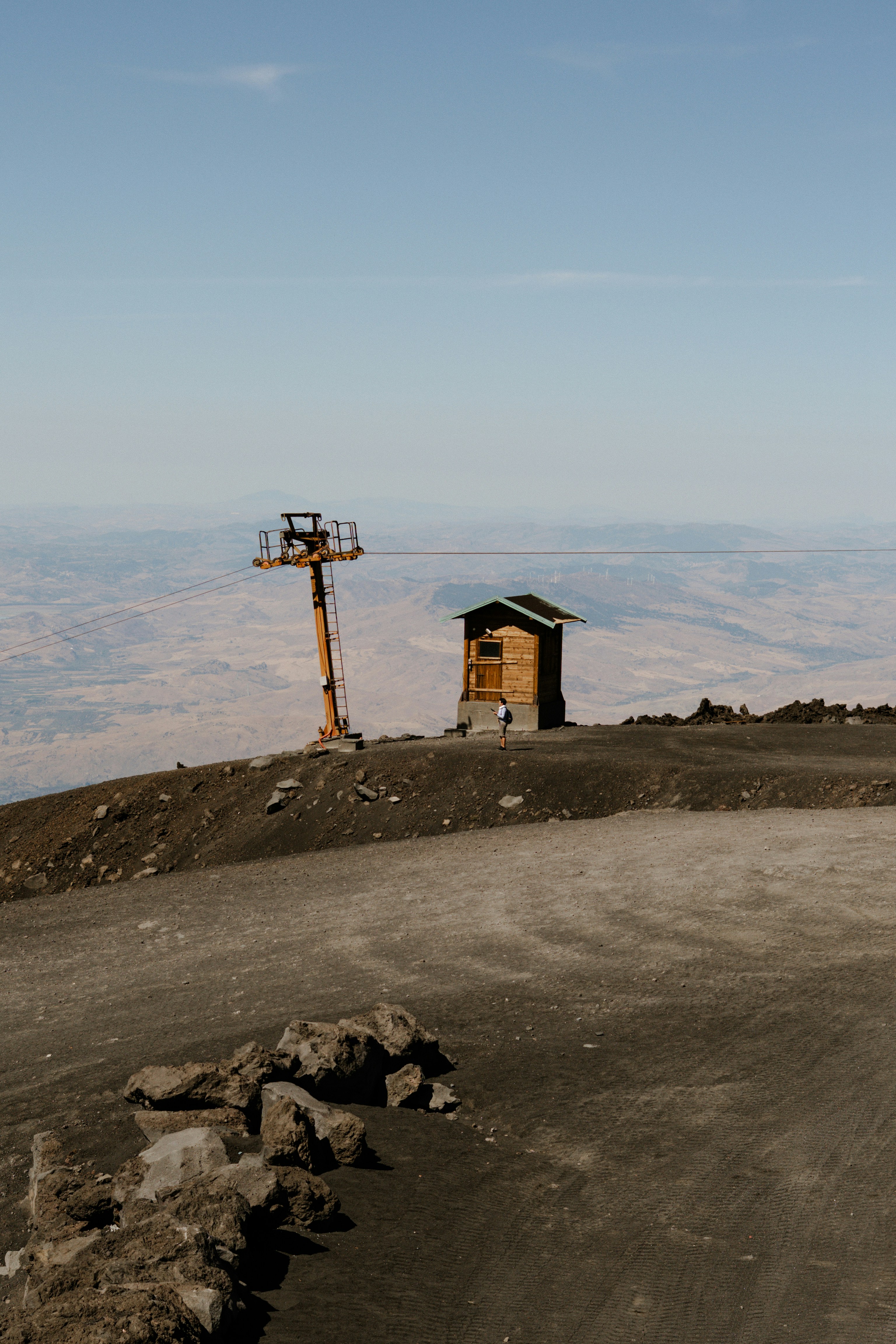 Wooden hut and ski lift on a barren mountainside.