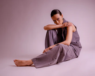 A woman in a grey suit sits on the floor.