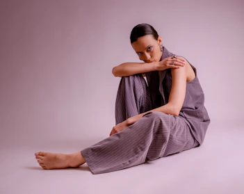 A woman in a grey suit sits on the floor.