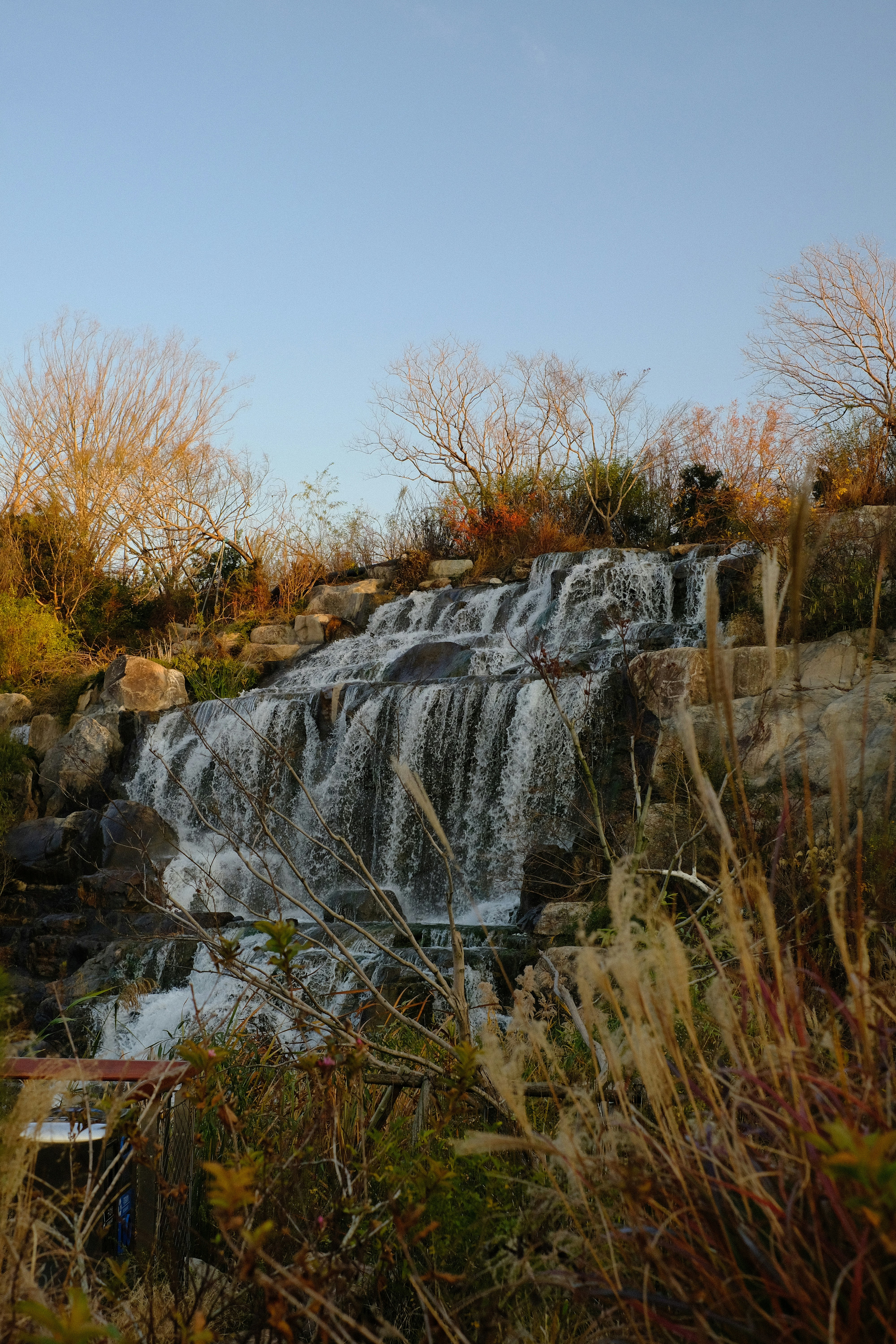 A cascading waterfall flows over rocks with dry grass.