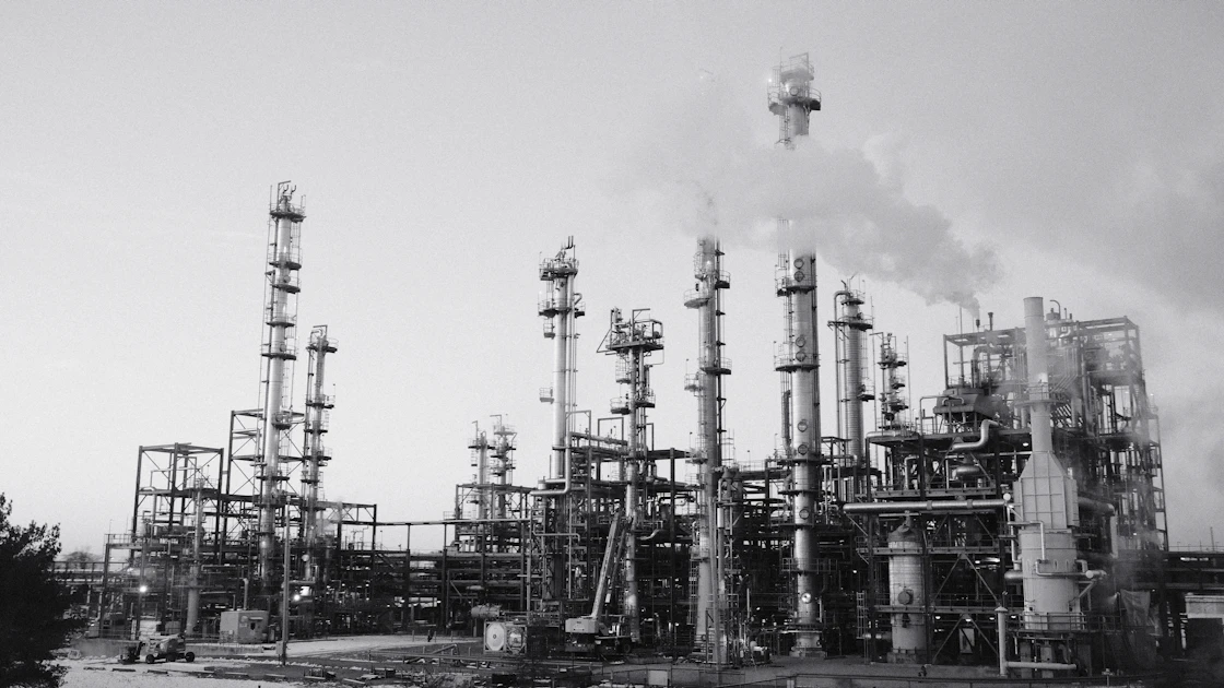 An industrial refinery with smoking stacks under a cloudy sky.