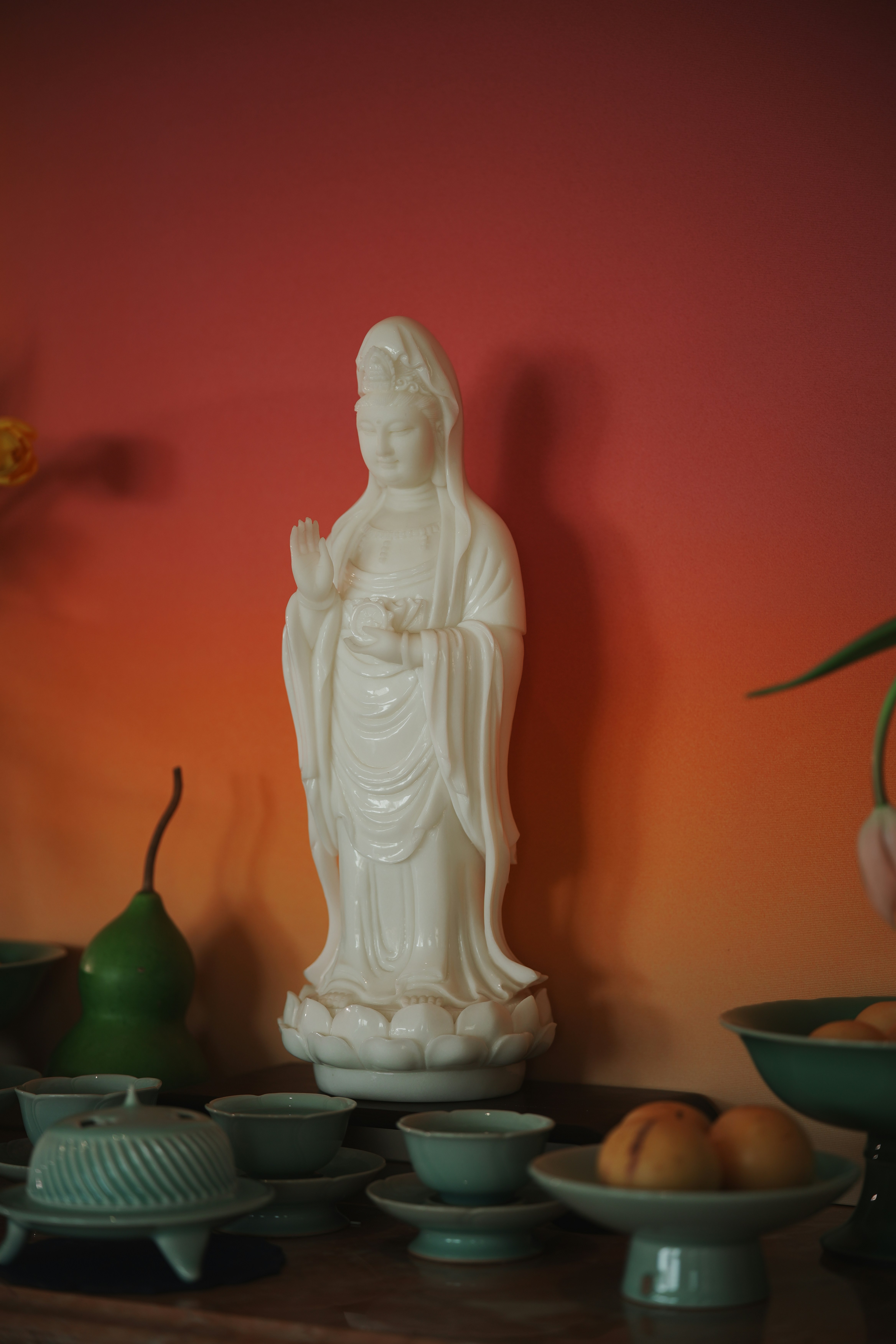White statue of a deity with offerings on a table.