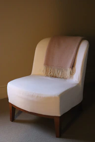 A white armchair with a pink blanket draped over it.
