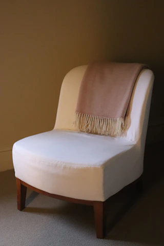 A white armchair with a pink blanket draped over it.