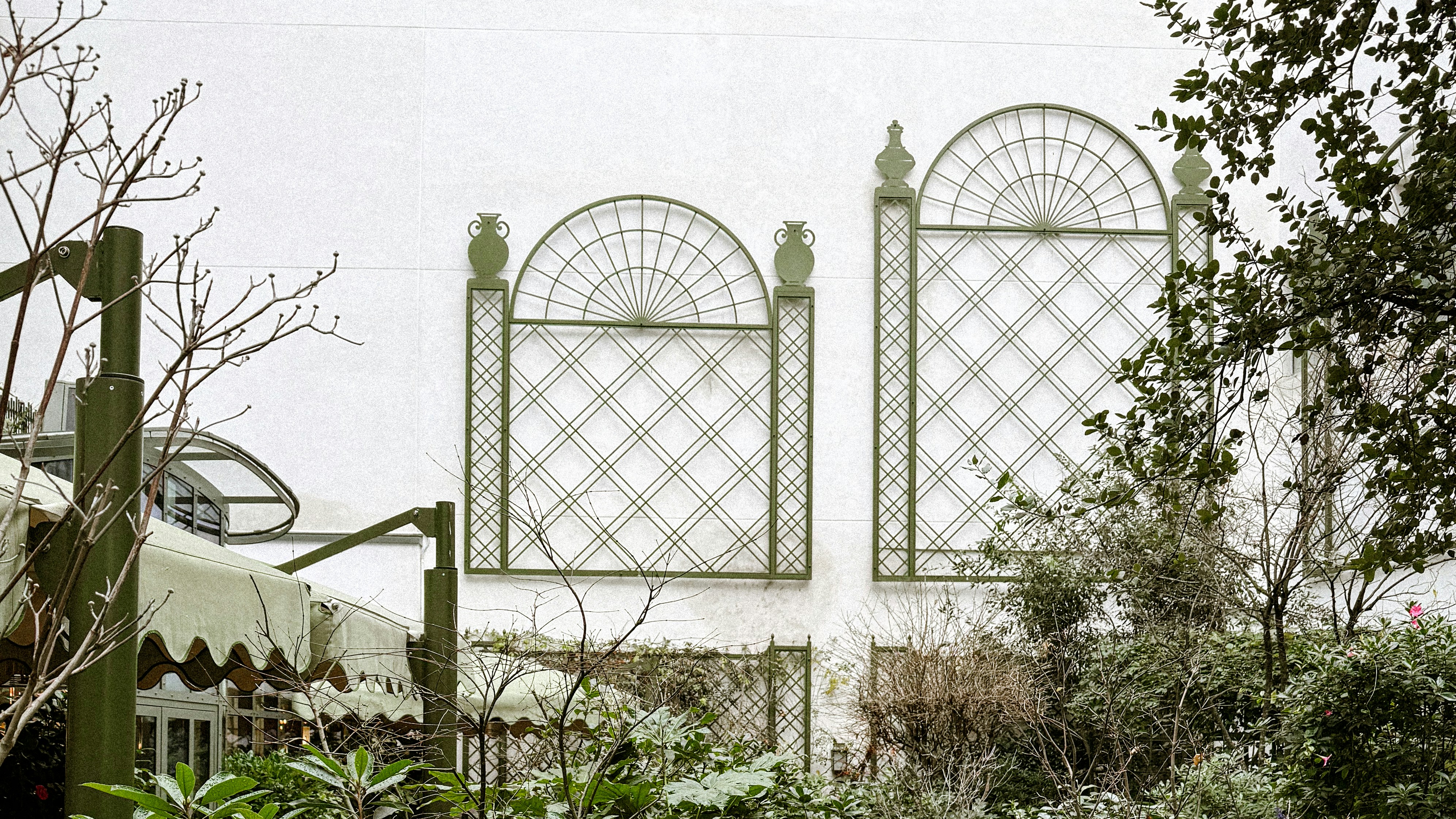 Two decorative windows on a white wall with greenery.
