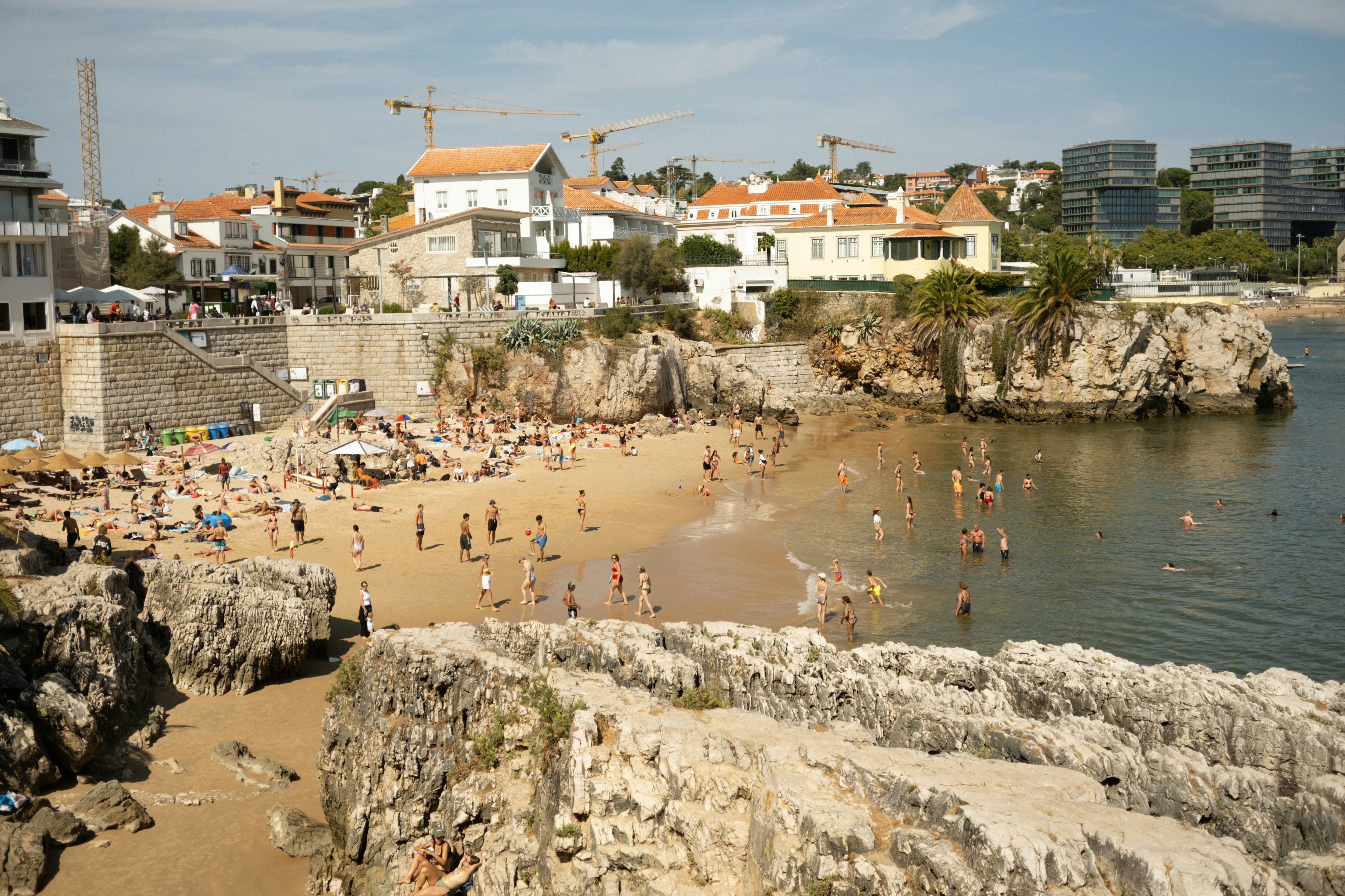 Crowded beach with rocky cliffs and buildings by the sea.