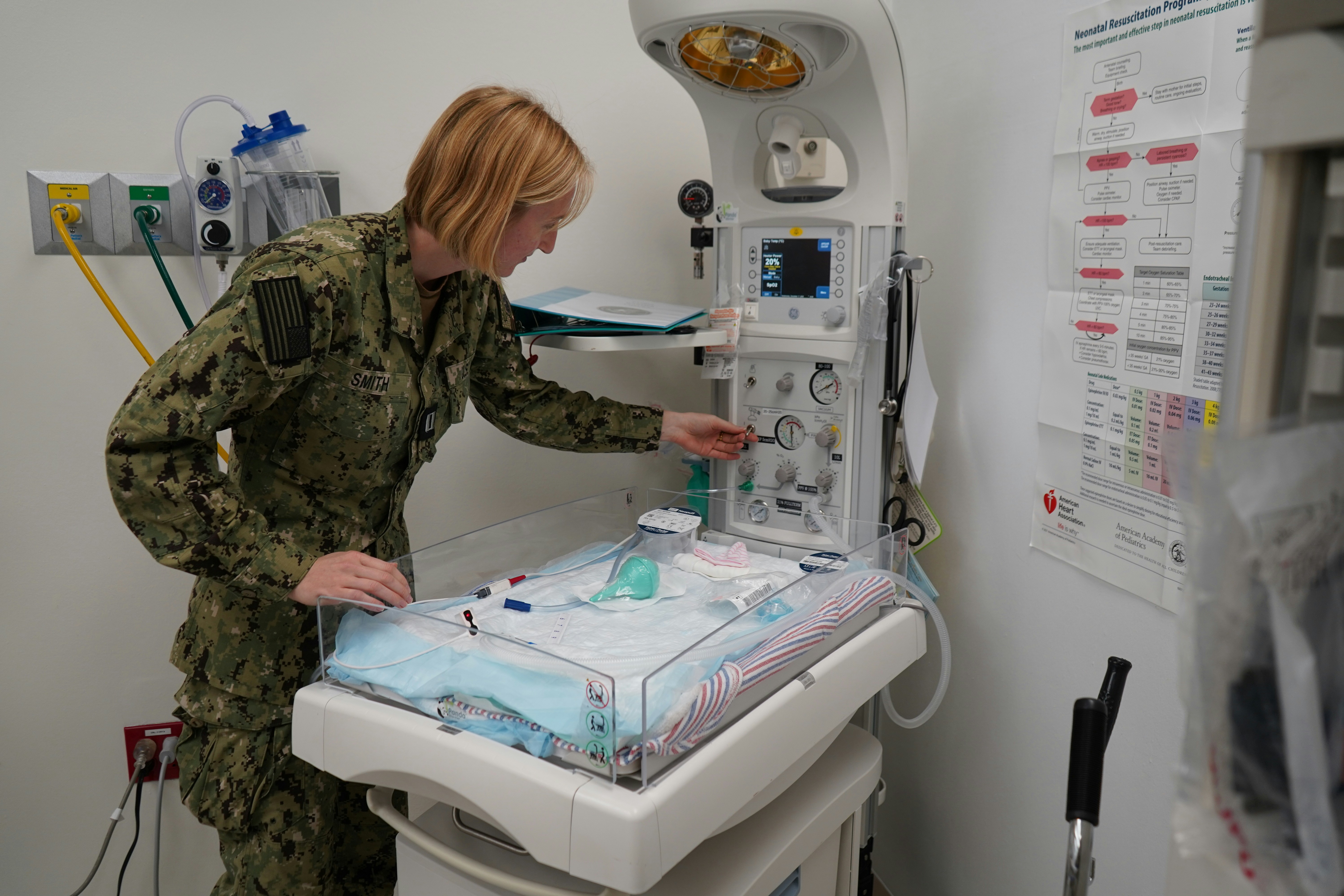 Nurse adjusts equipment at a baby's bedside.