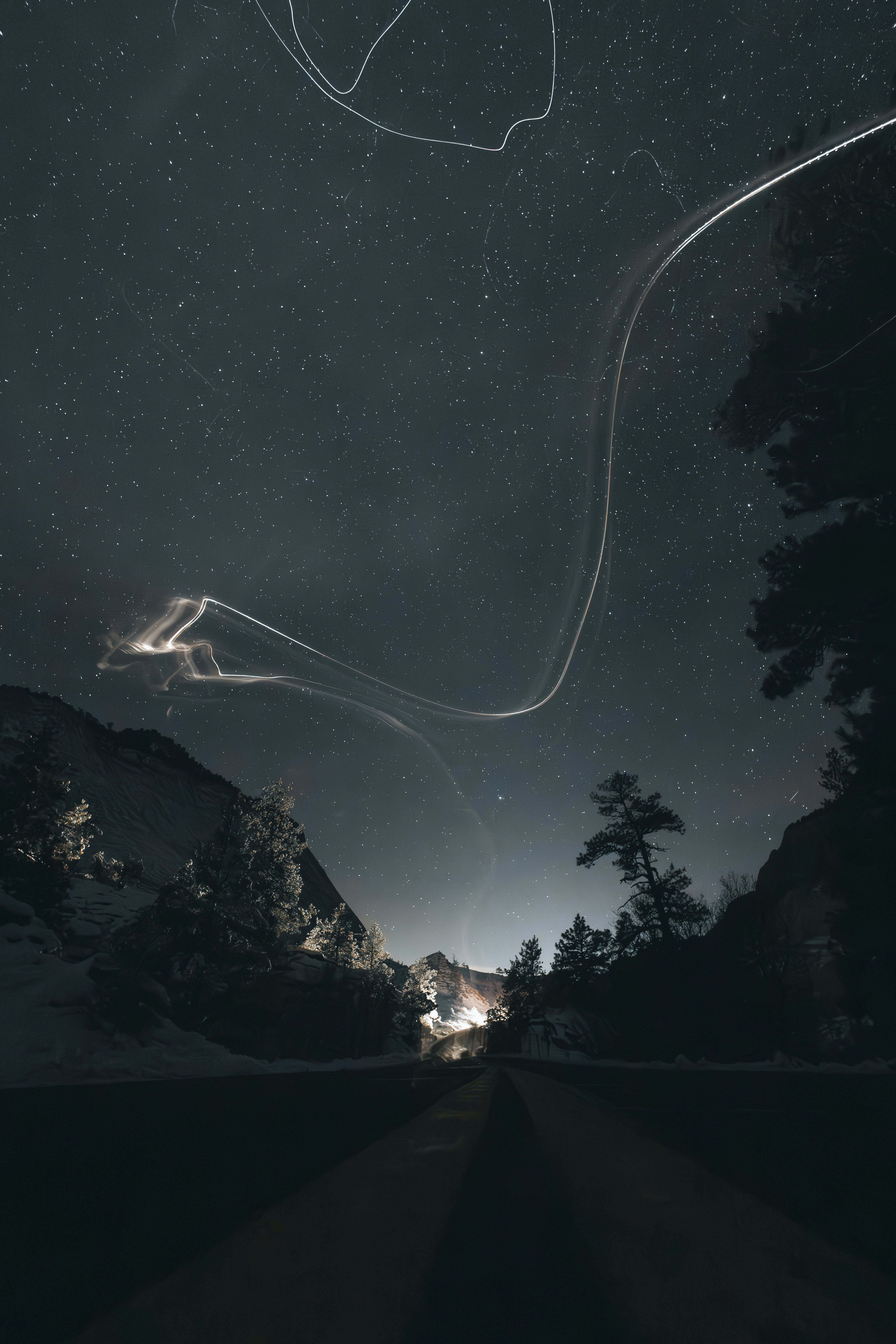 Light trails streak across a starry night sky over mountains.
