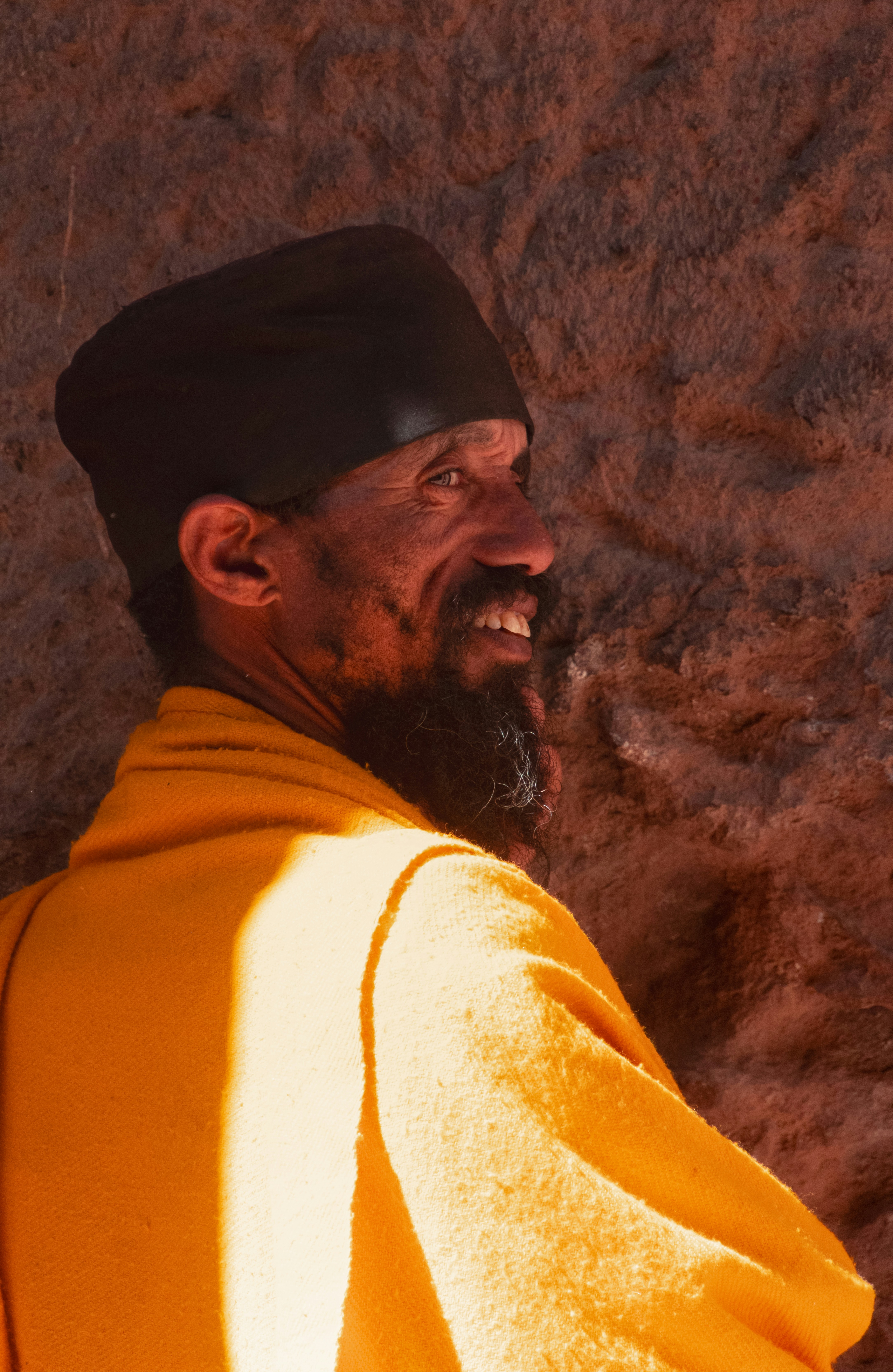 A smiling man in a black cap and yellow robe