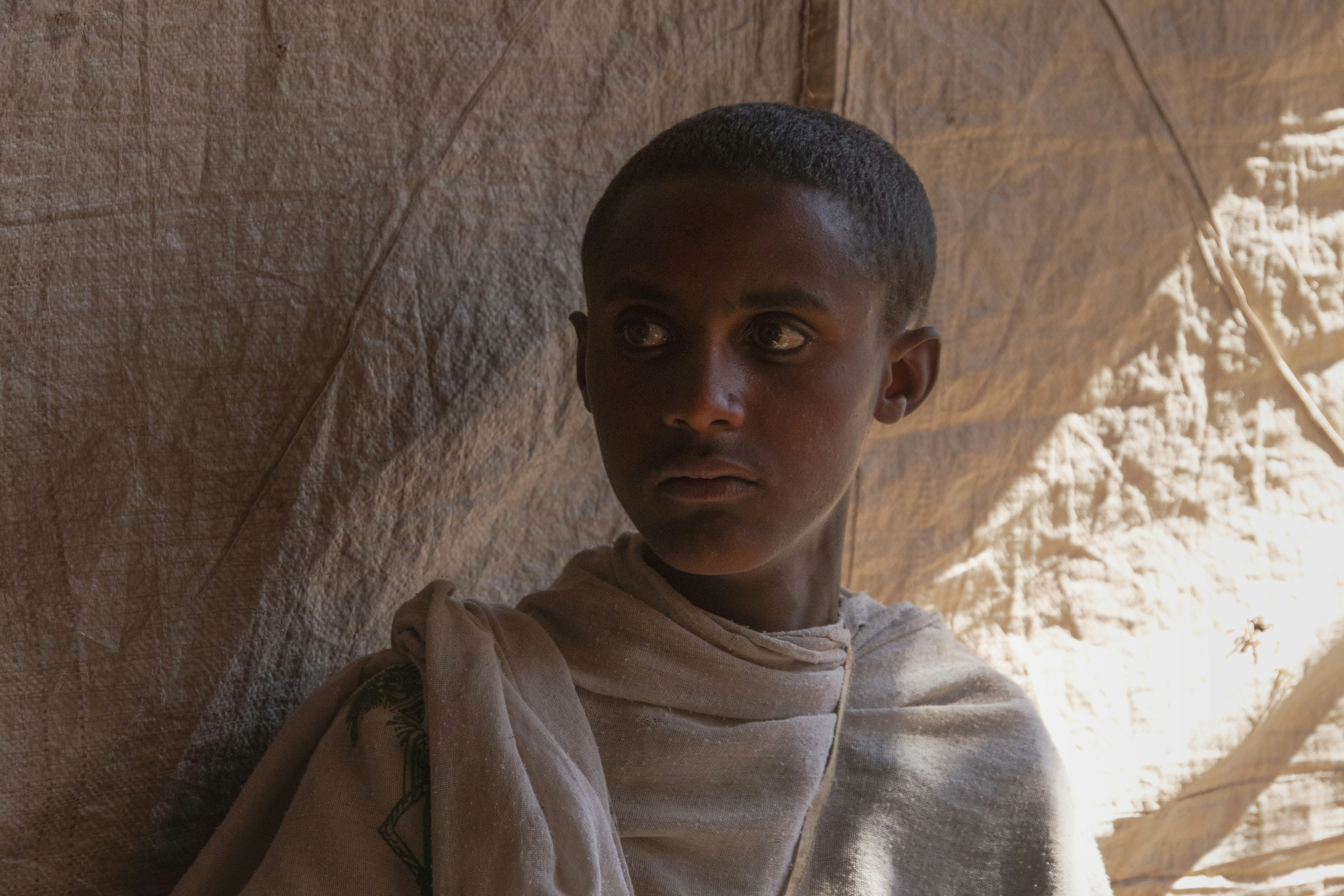 Young person in light-colored robes looks to the side