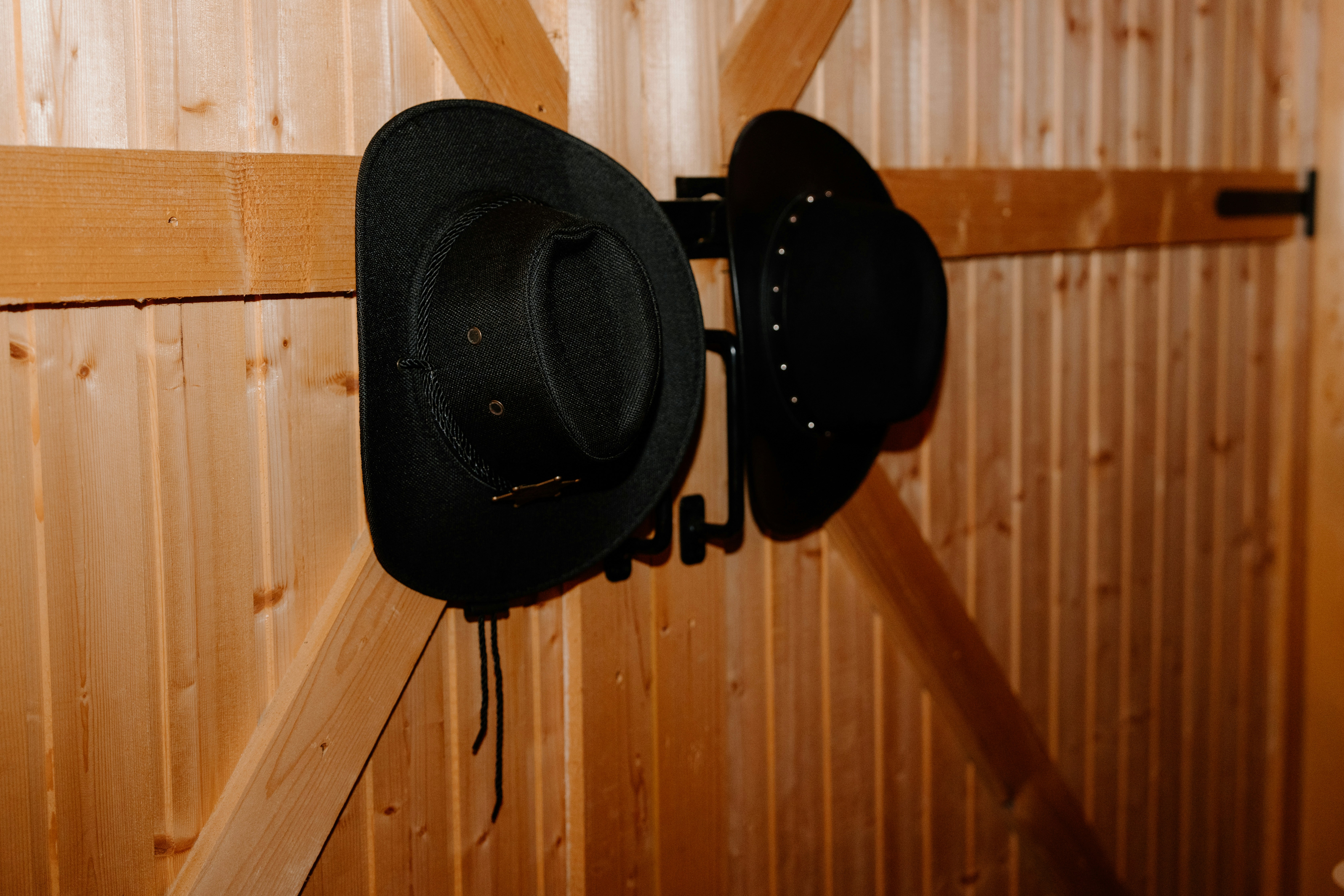 Zwei schwarze Cowboyhüte hängen an einer Holzwand