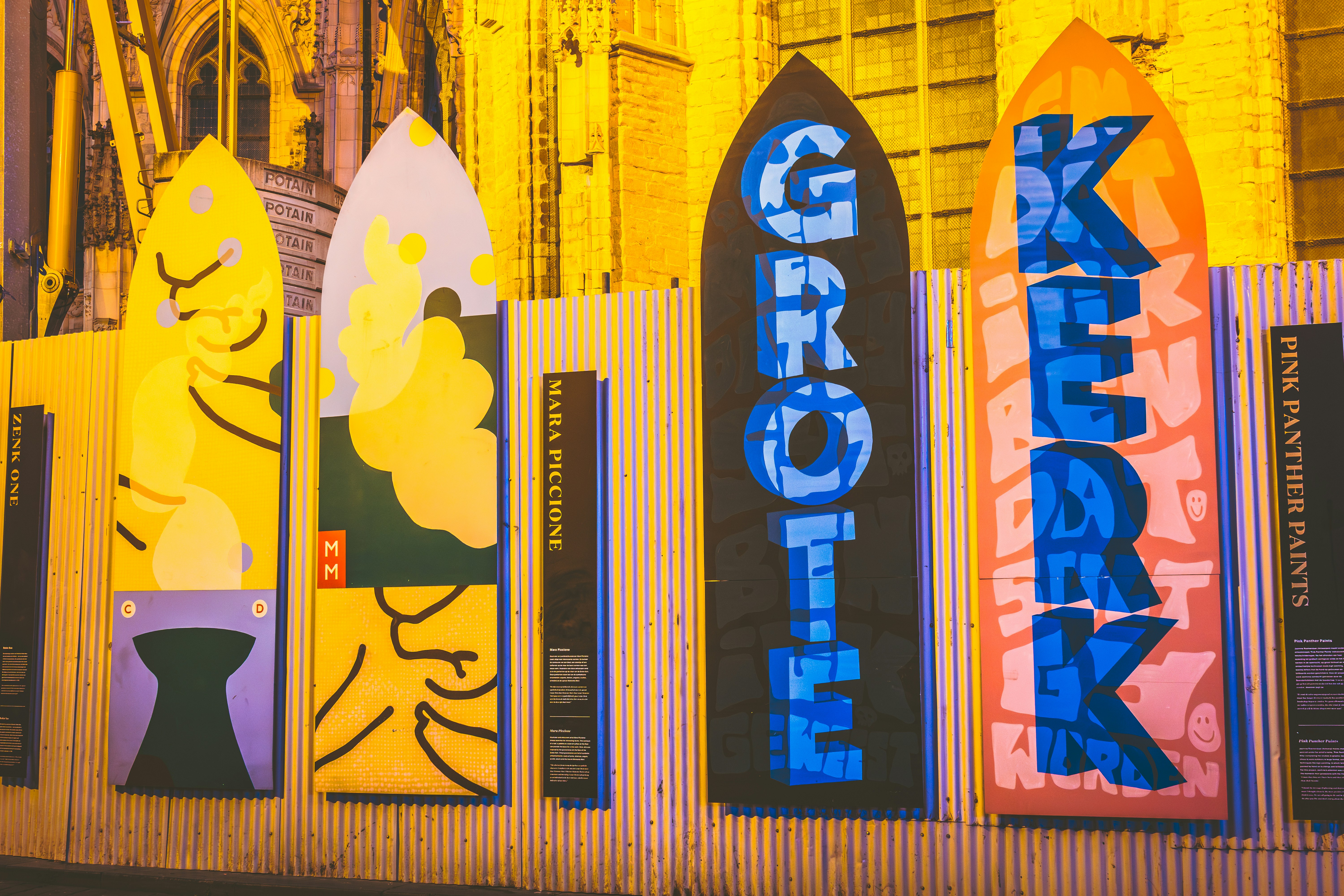 Colorful signs spell out 'grote kerk' on a fence.