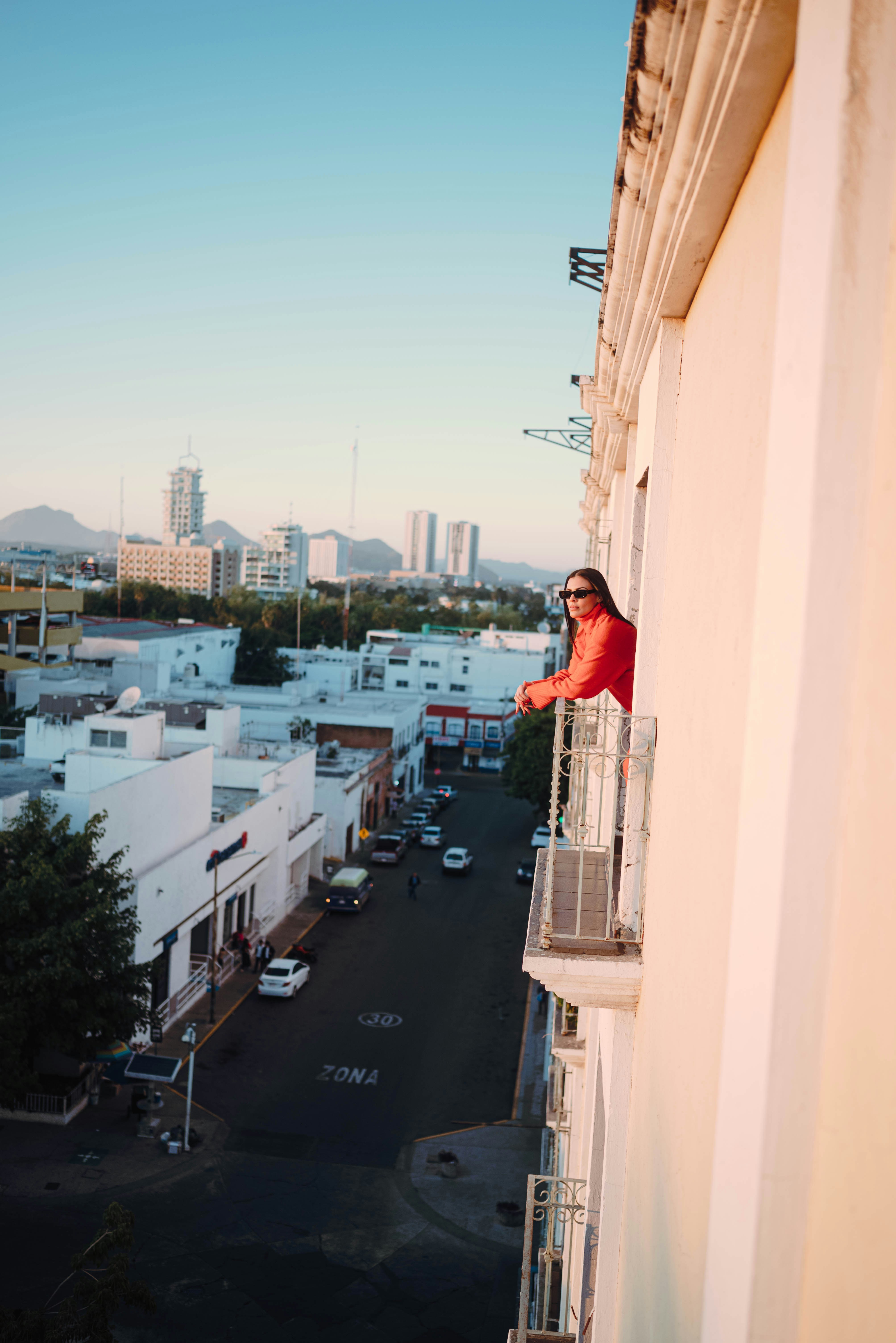 Woman on balcony overlooking city street at sunset
