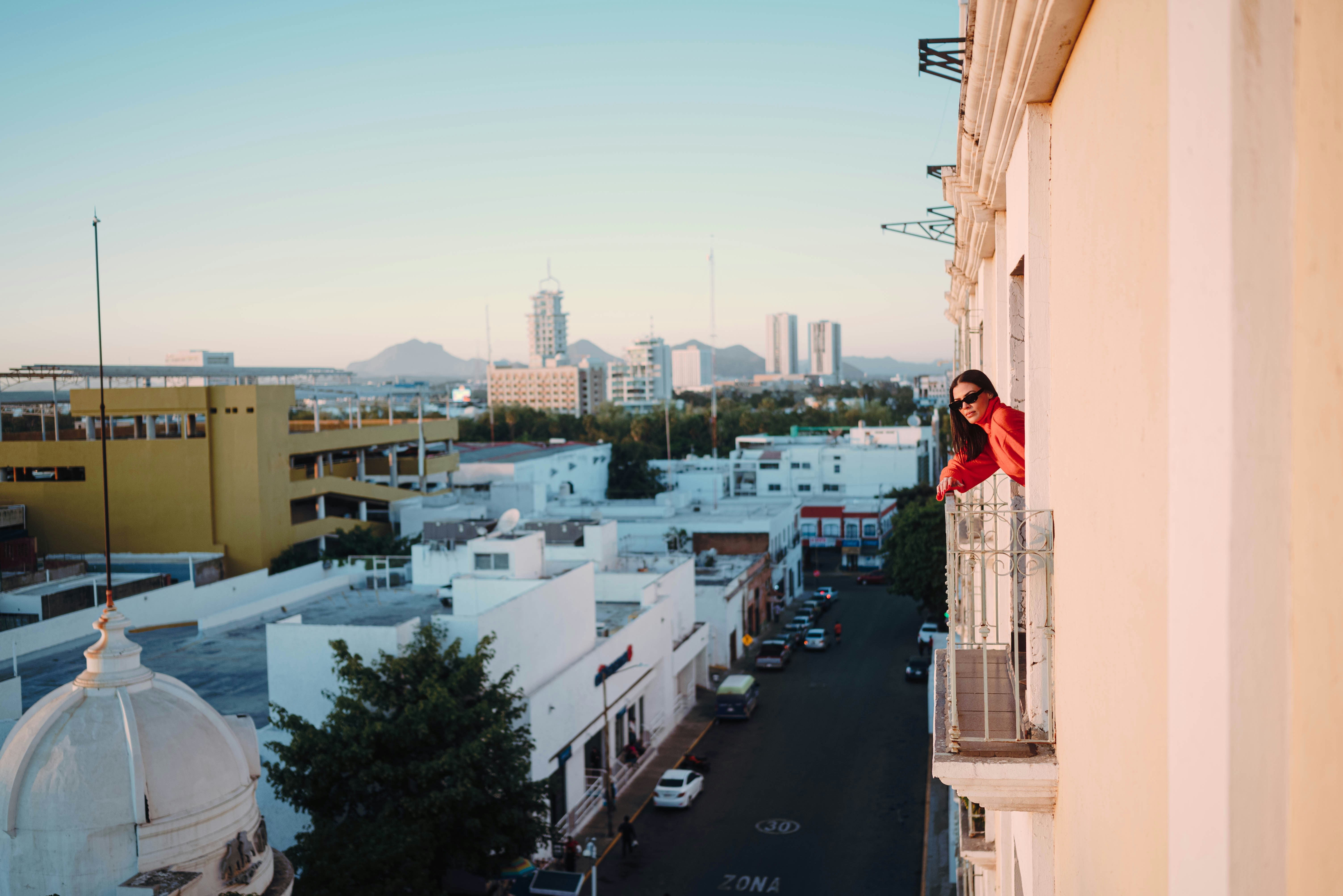 Woman leaning out of a balcony overlooking a city street.