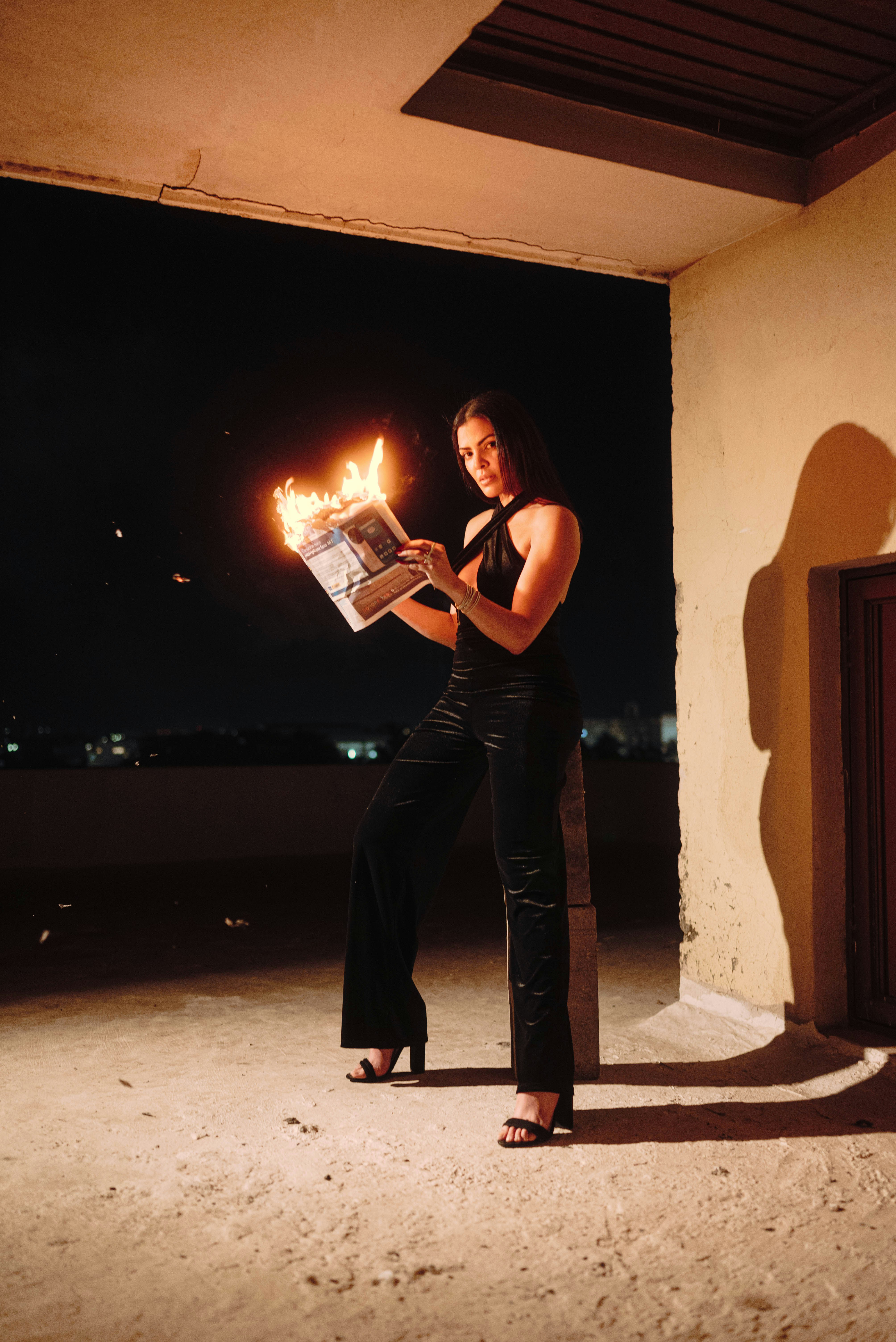 Woman in black dress holding burning newspaper at night