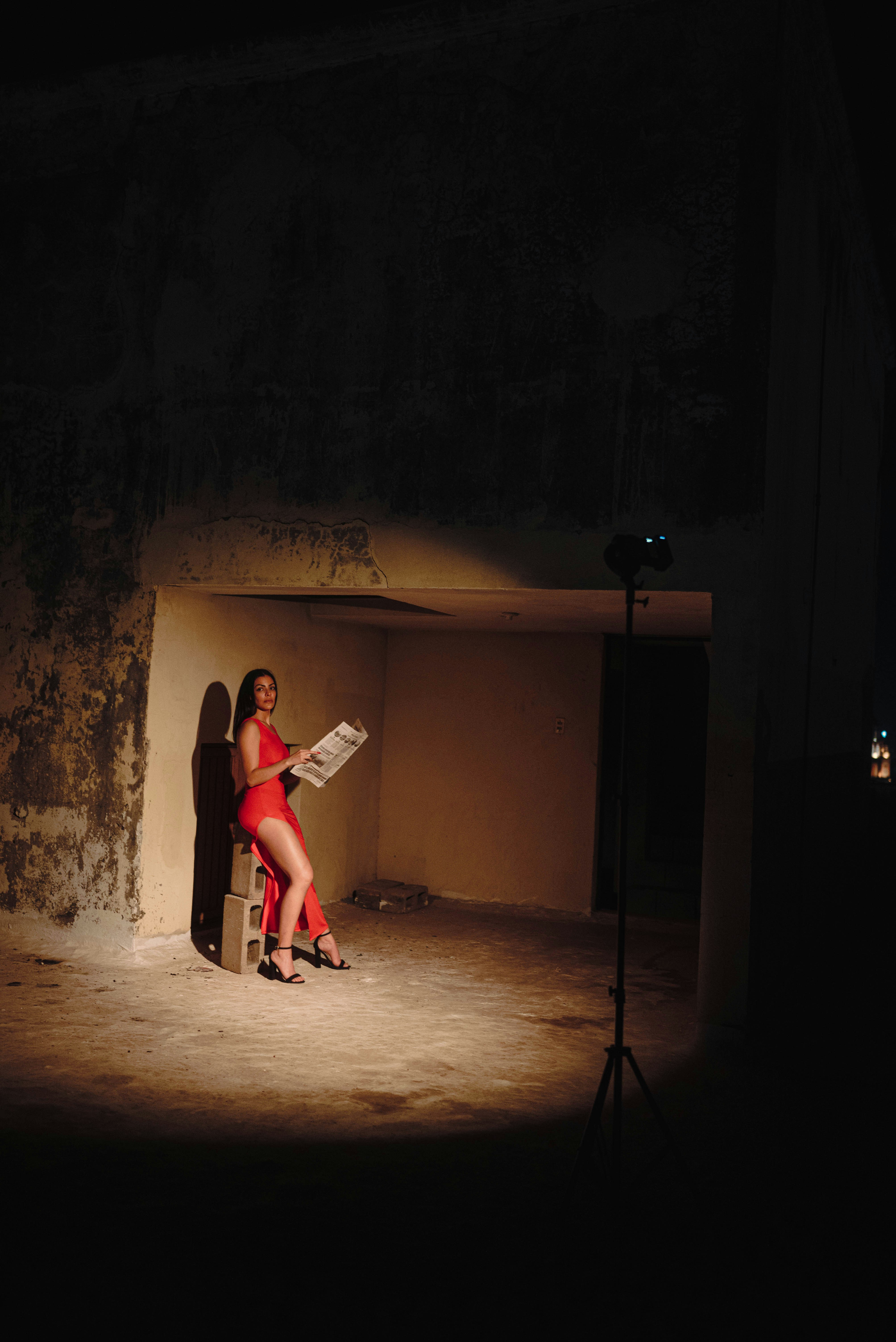 Woman in red dress reading newspaper in dimly lit room.
