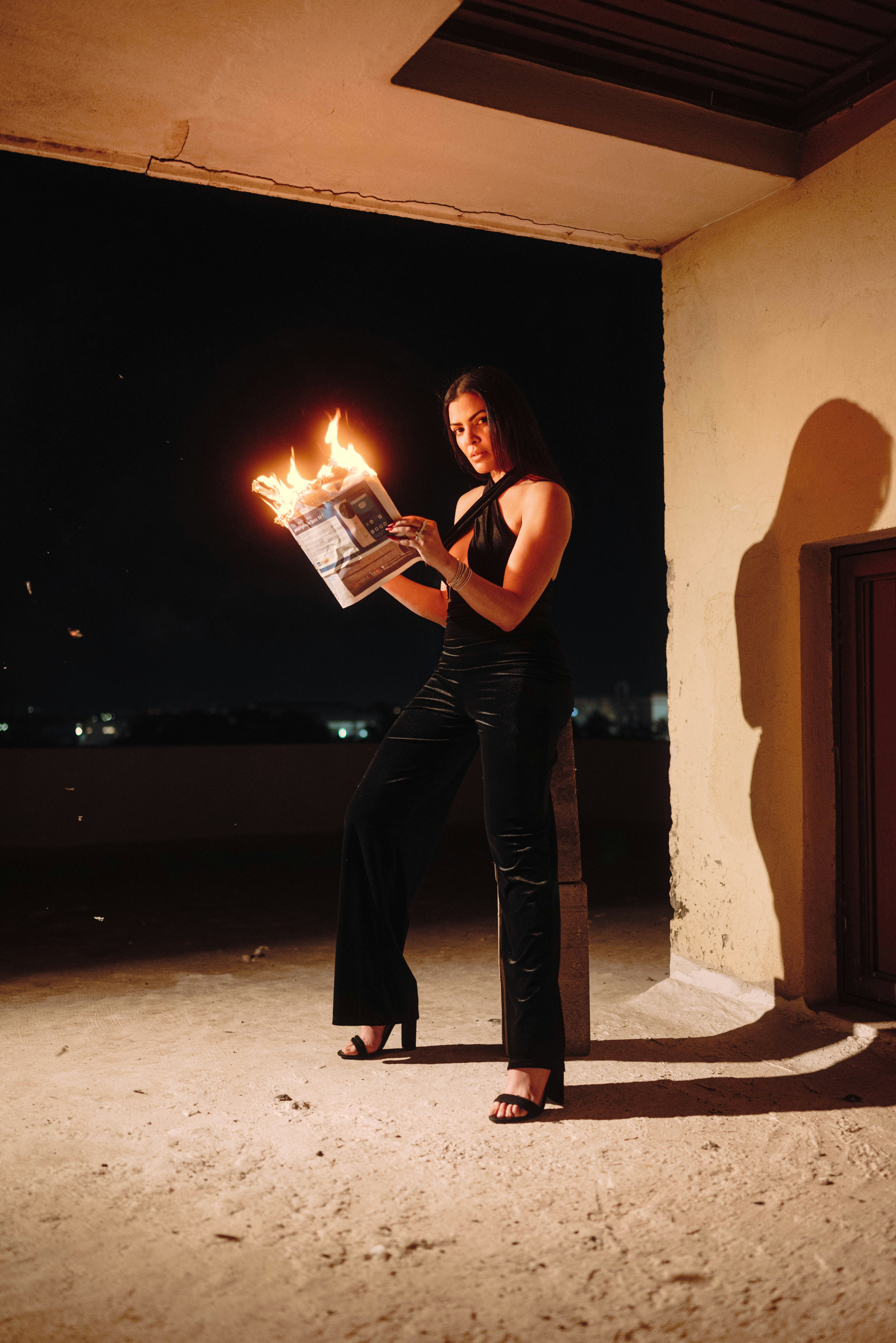 Woman in black holding burning newspaper at night
