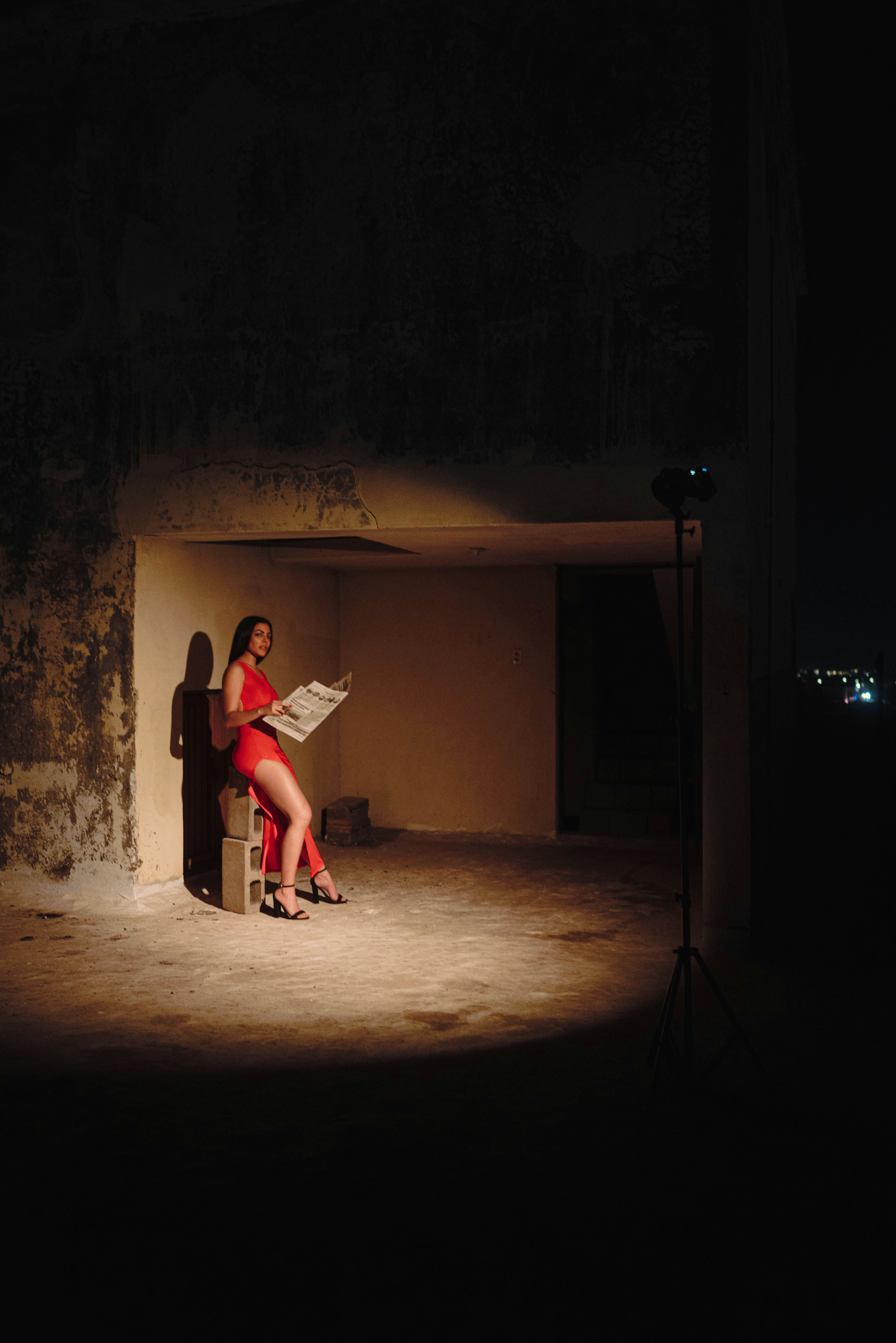 Woman in red dress reading newspaper in dimly lit room.