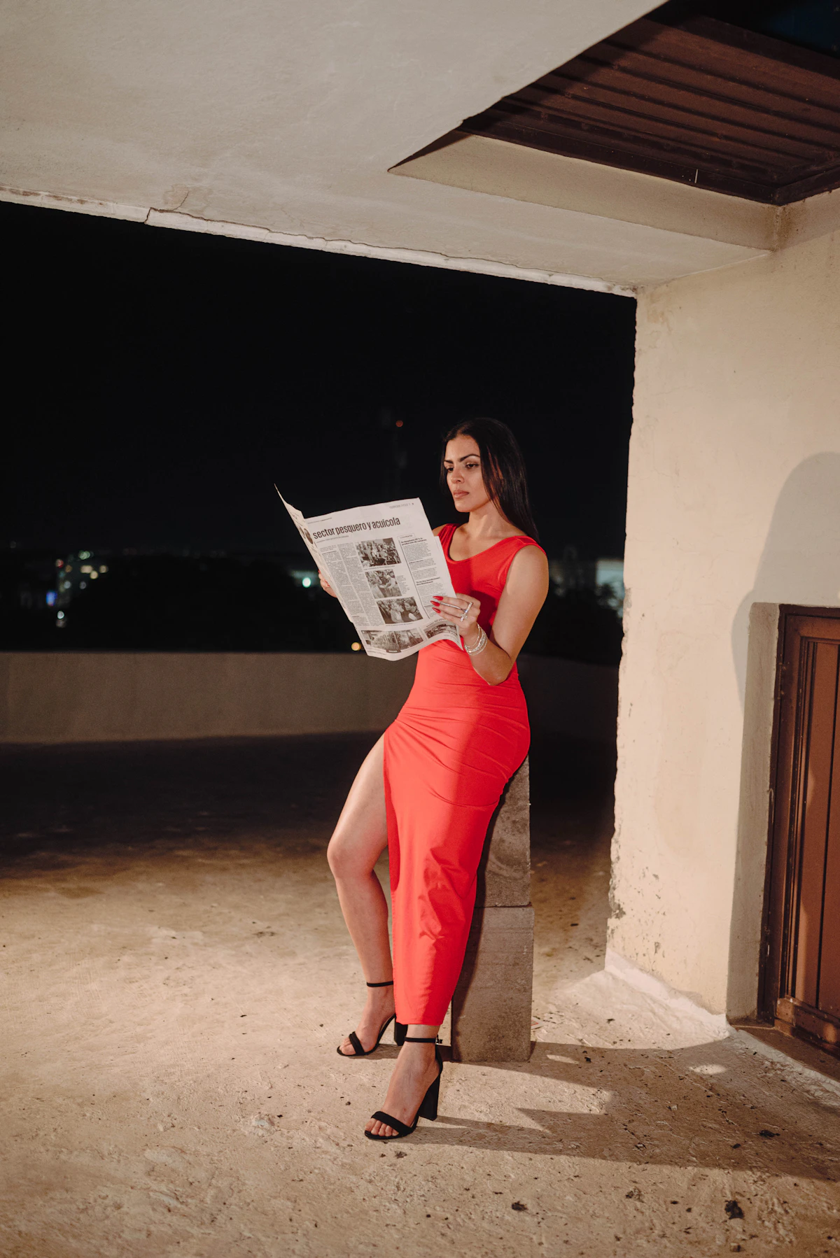 A woman in a red dress reading a newspaper under a streetlight