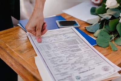 Person pointing at a marriage certificate on a wooden table.