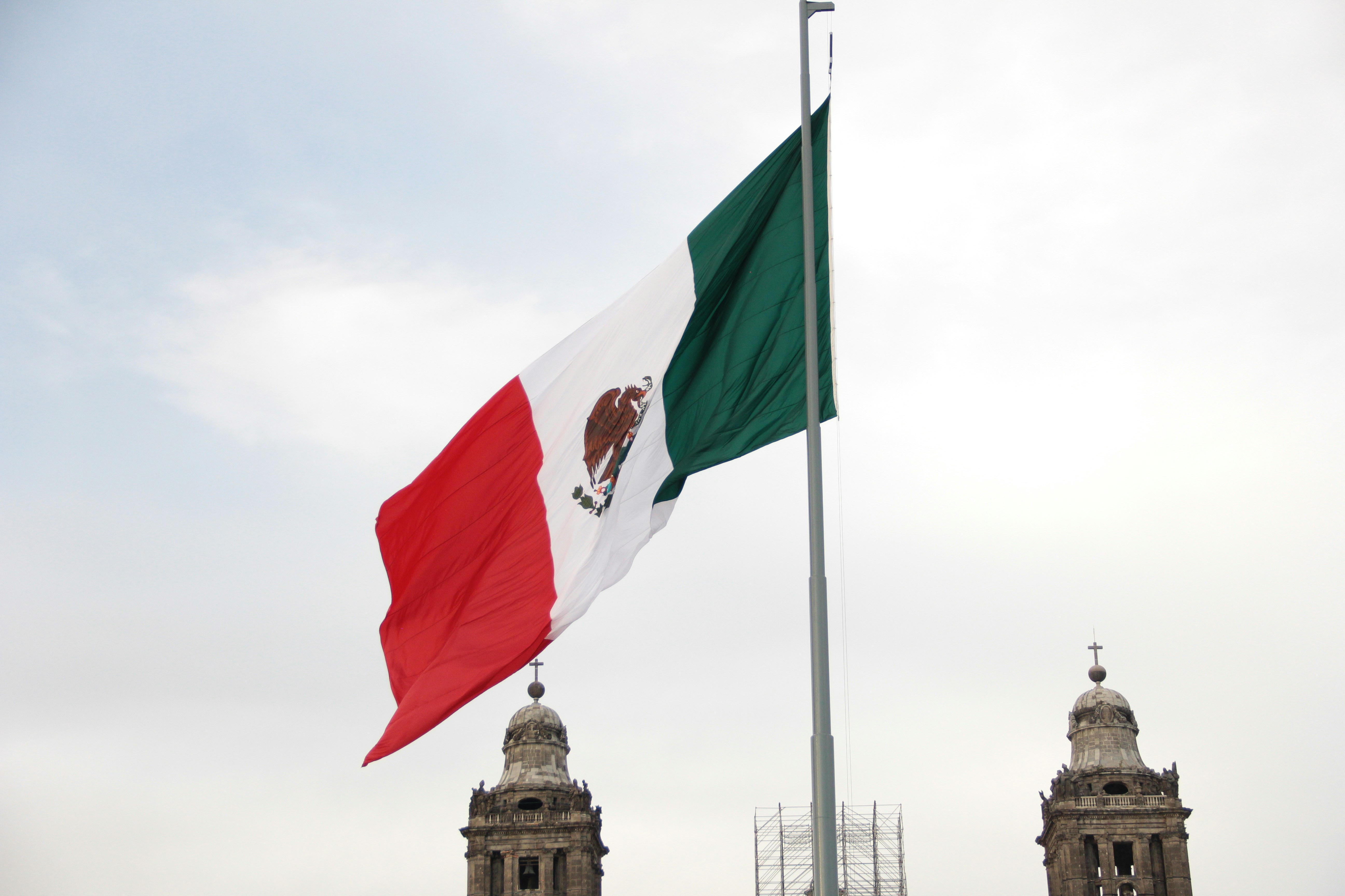The mexican flag flies proudly against a cloudy sky.