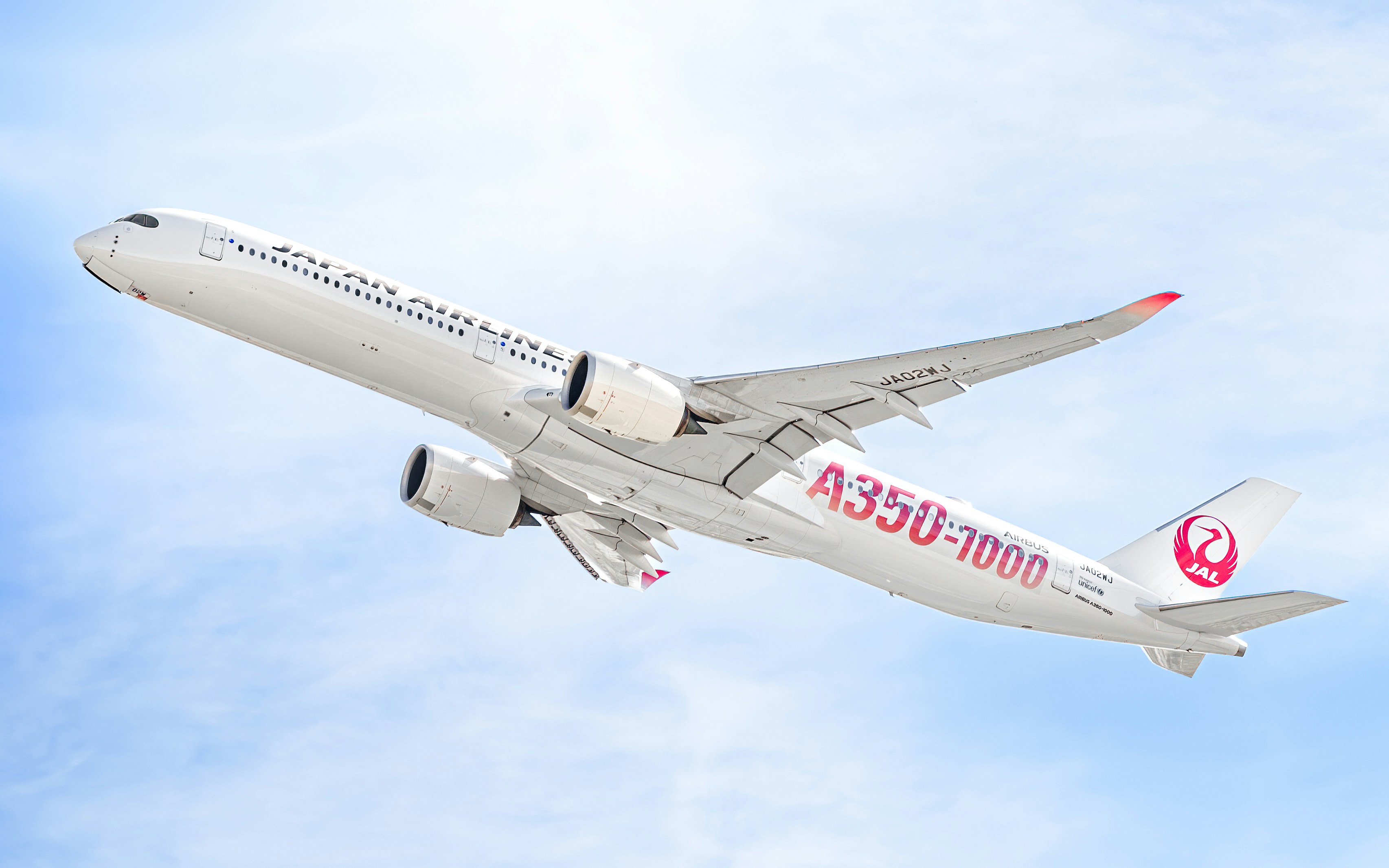 Ein weißes Flugzeug mit roten Buchstaben fliegt am Himmel.