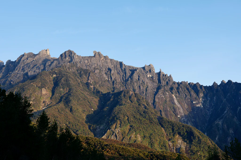 Jagged granite peaks of Mount Kinabalu above forested slopes under a clear blue sky