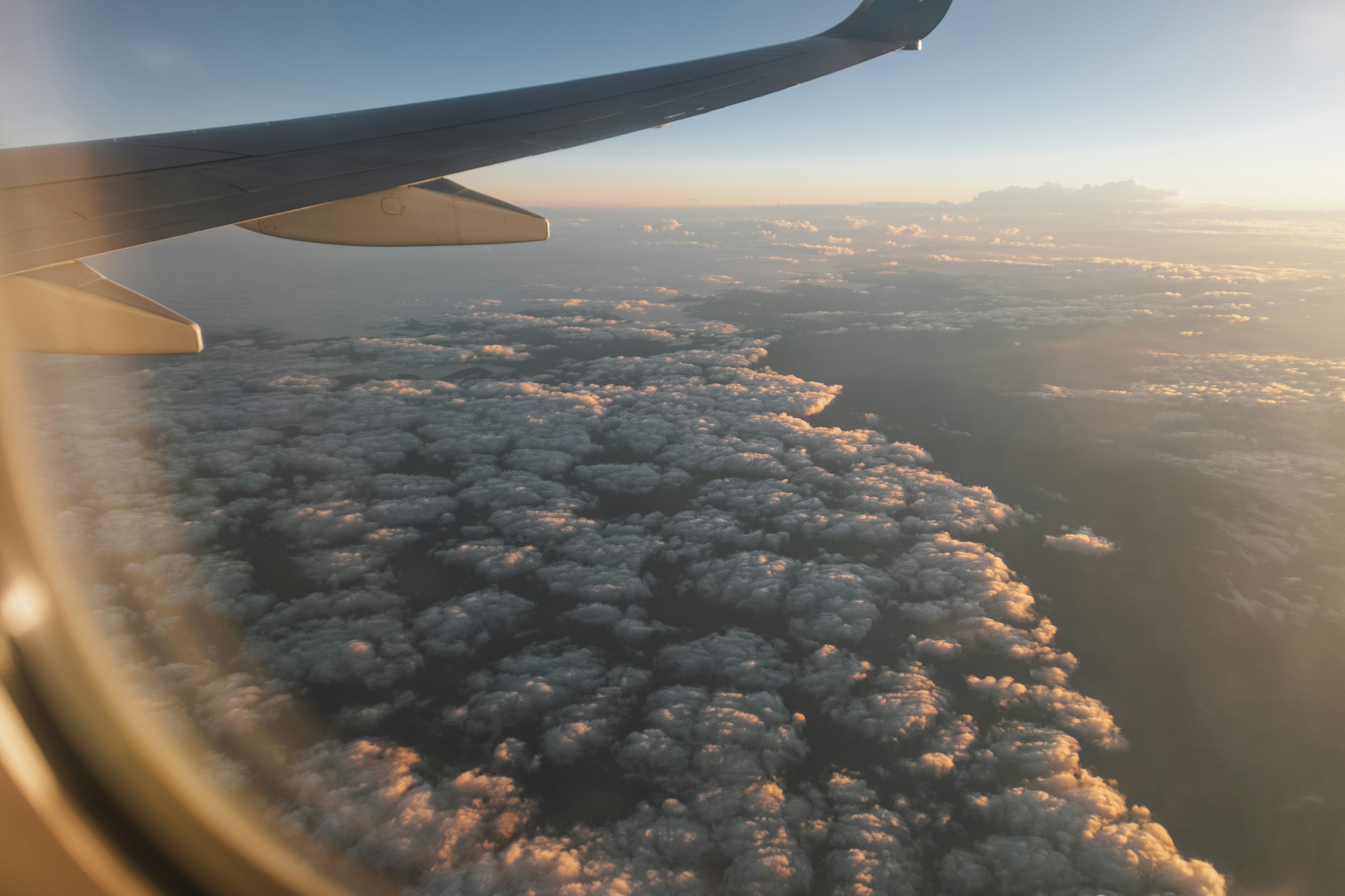 Airplane wing above fluffy clouds at sunset