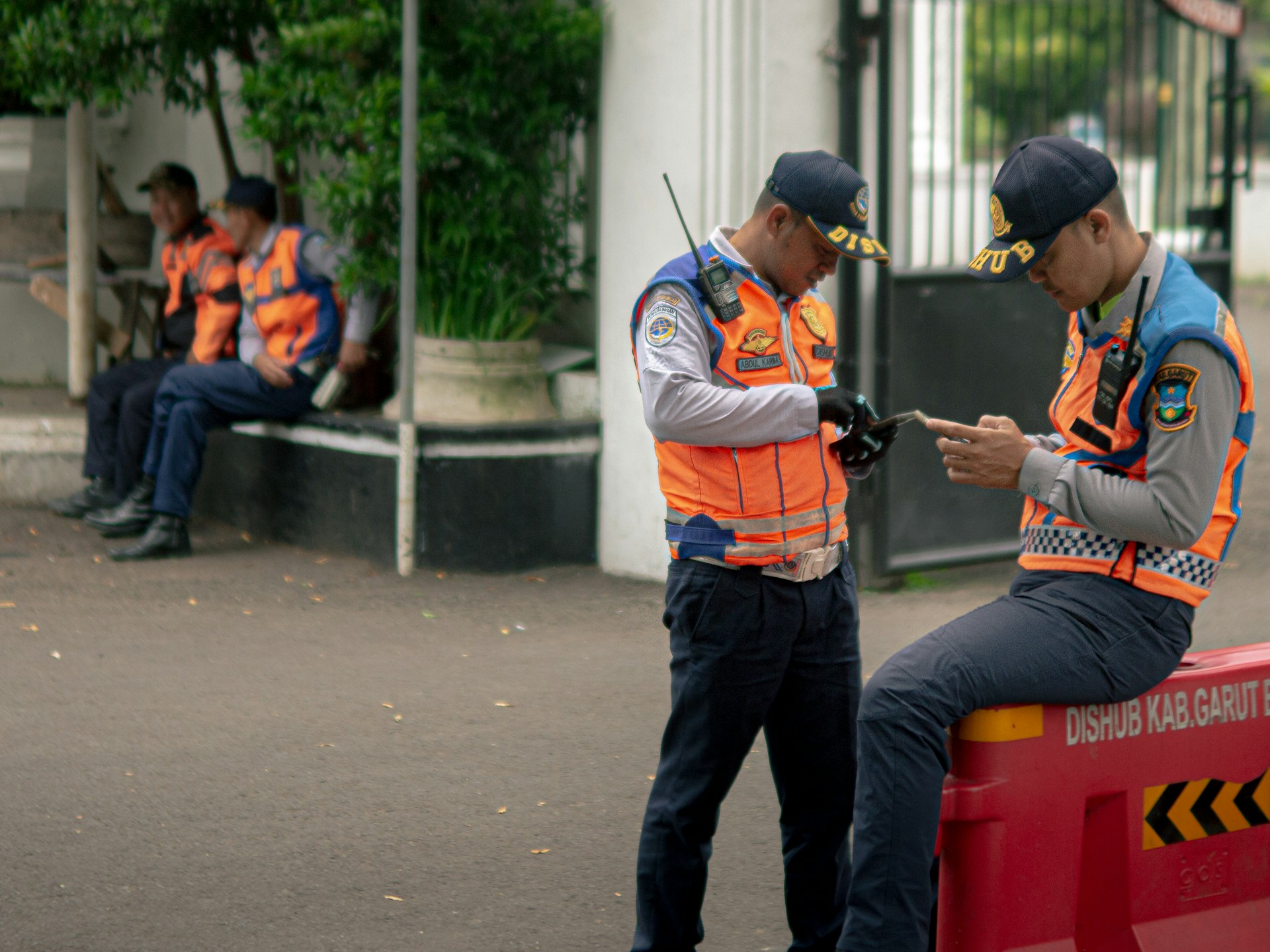 Two traffic officers in orange vests check their phones.