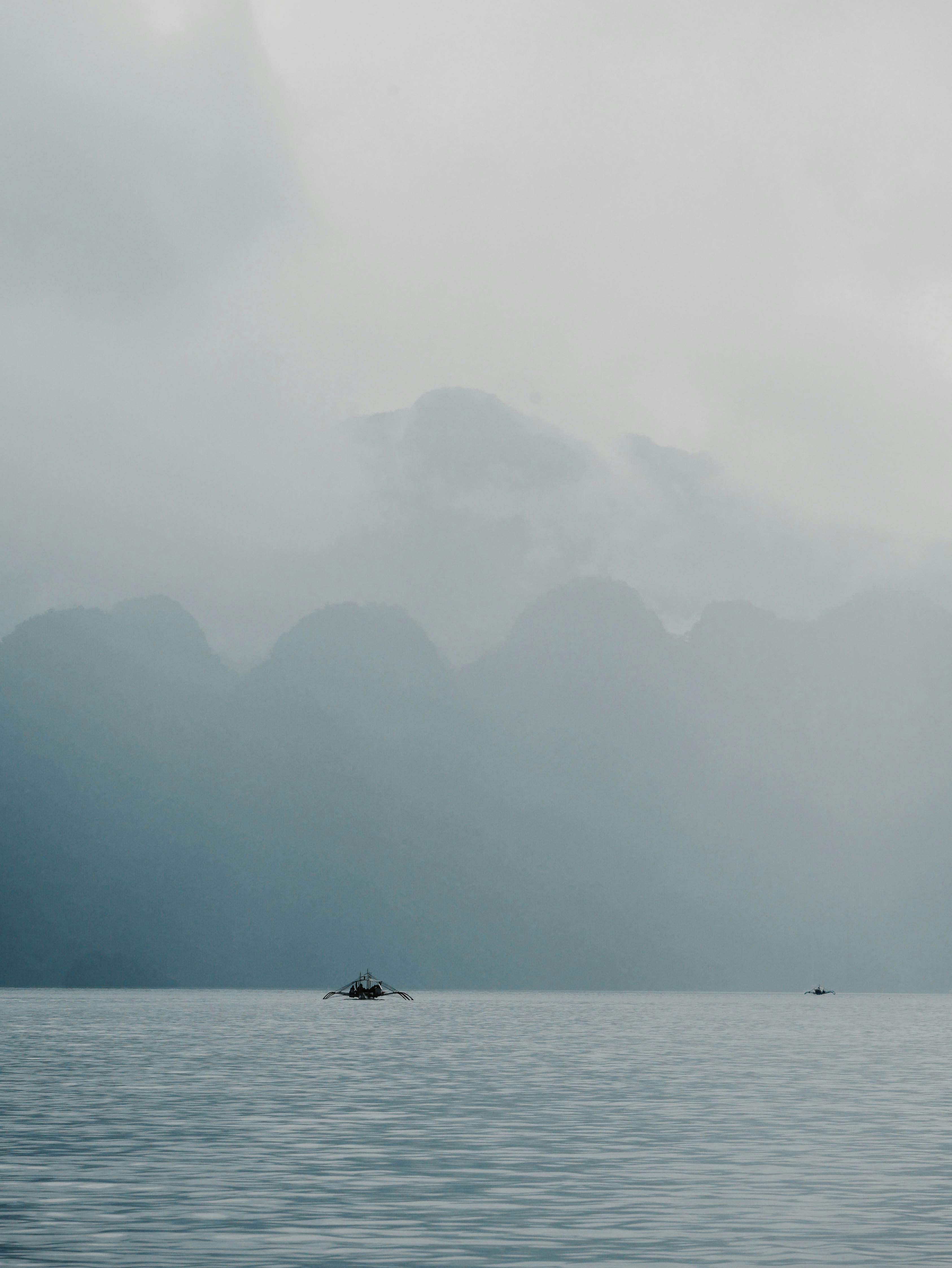 A small boat on the water with misty mountains behind.