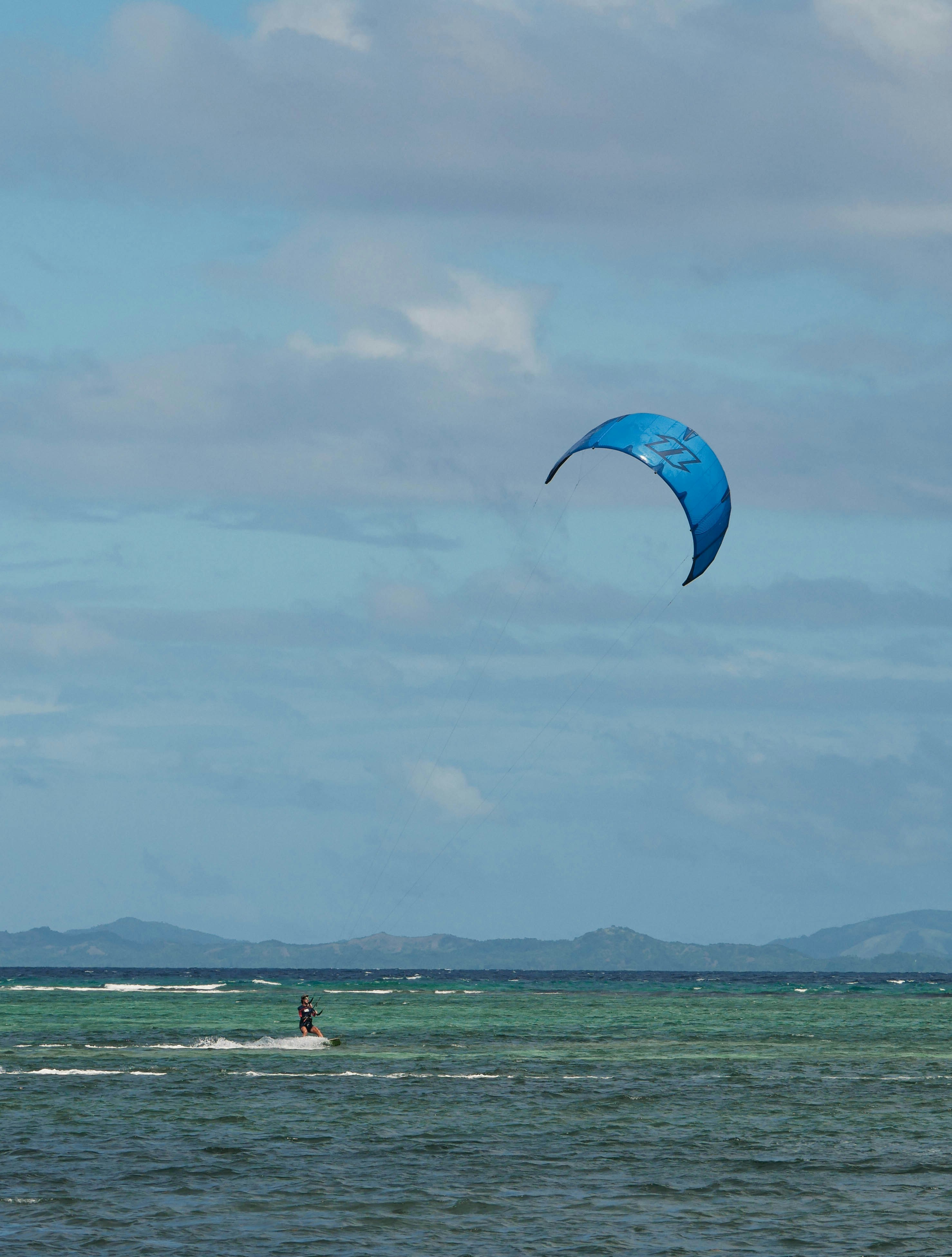 A person kitesurfing under a blue sky with clouds.