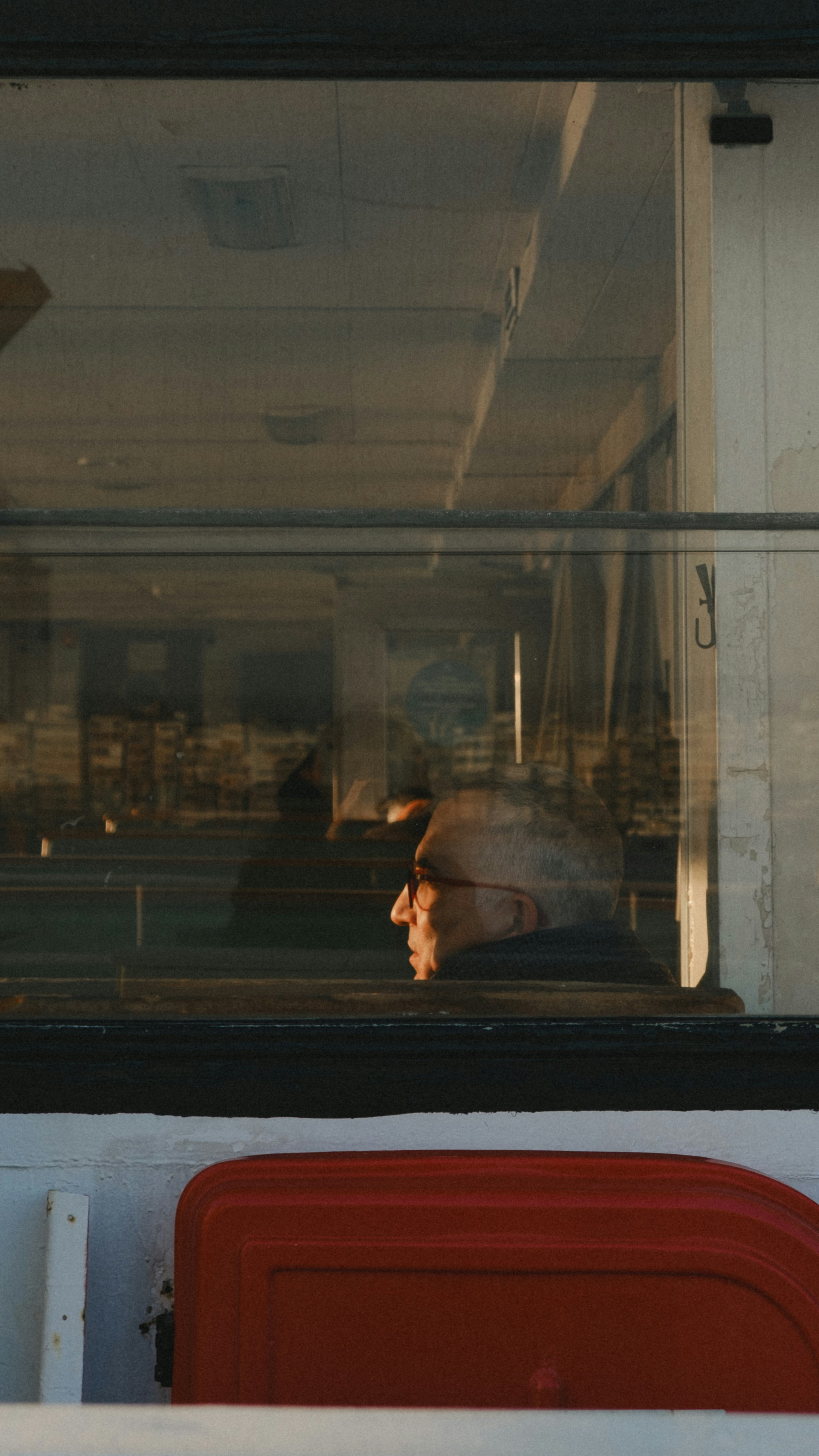 Mann im Profil spiegelt sich im Fenster mit rotem Objekt darunter