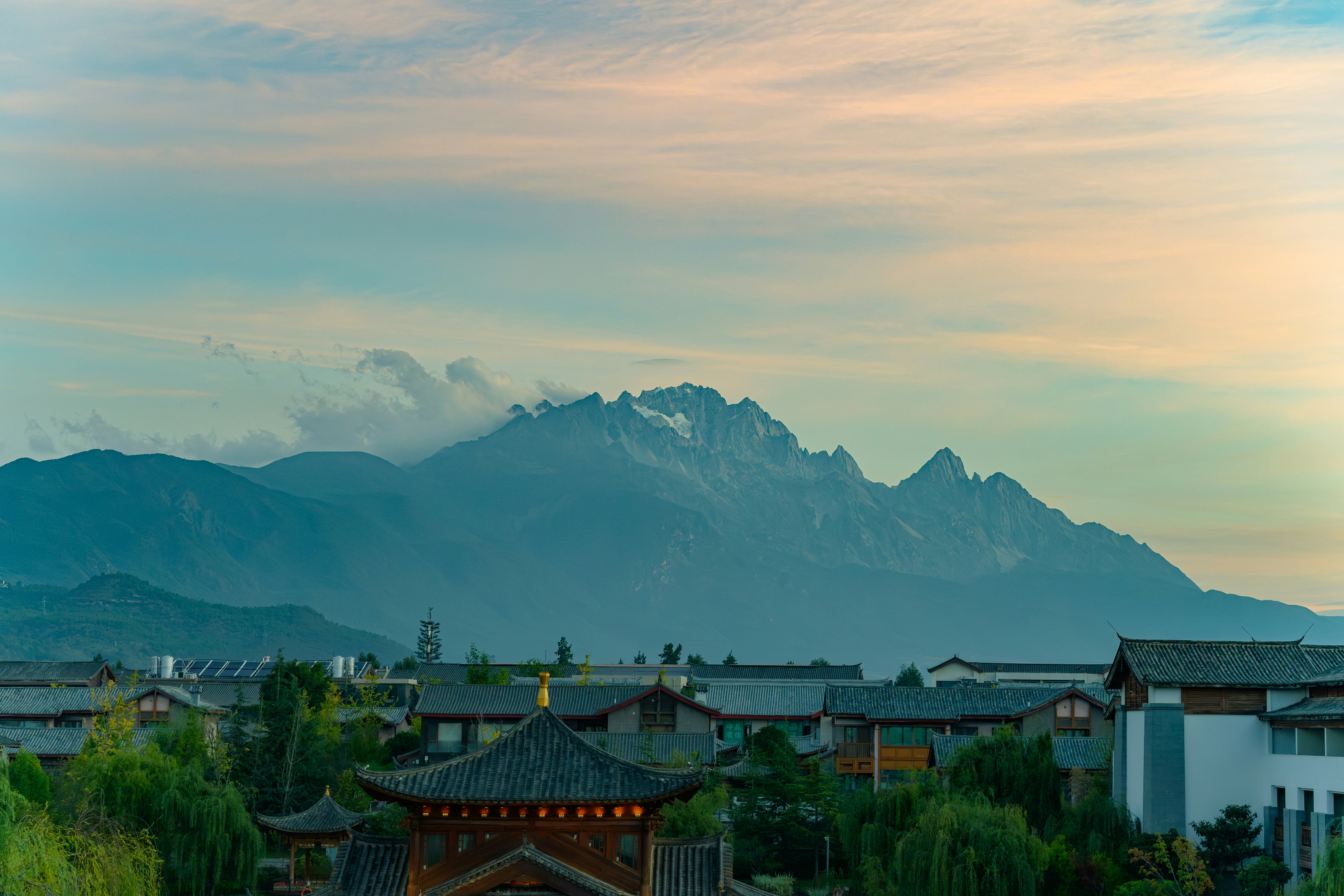 Snow-capped mountains loom over a village at dusk.