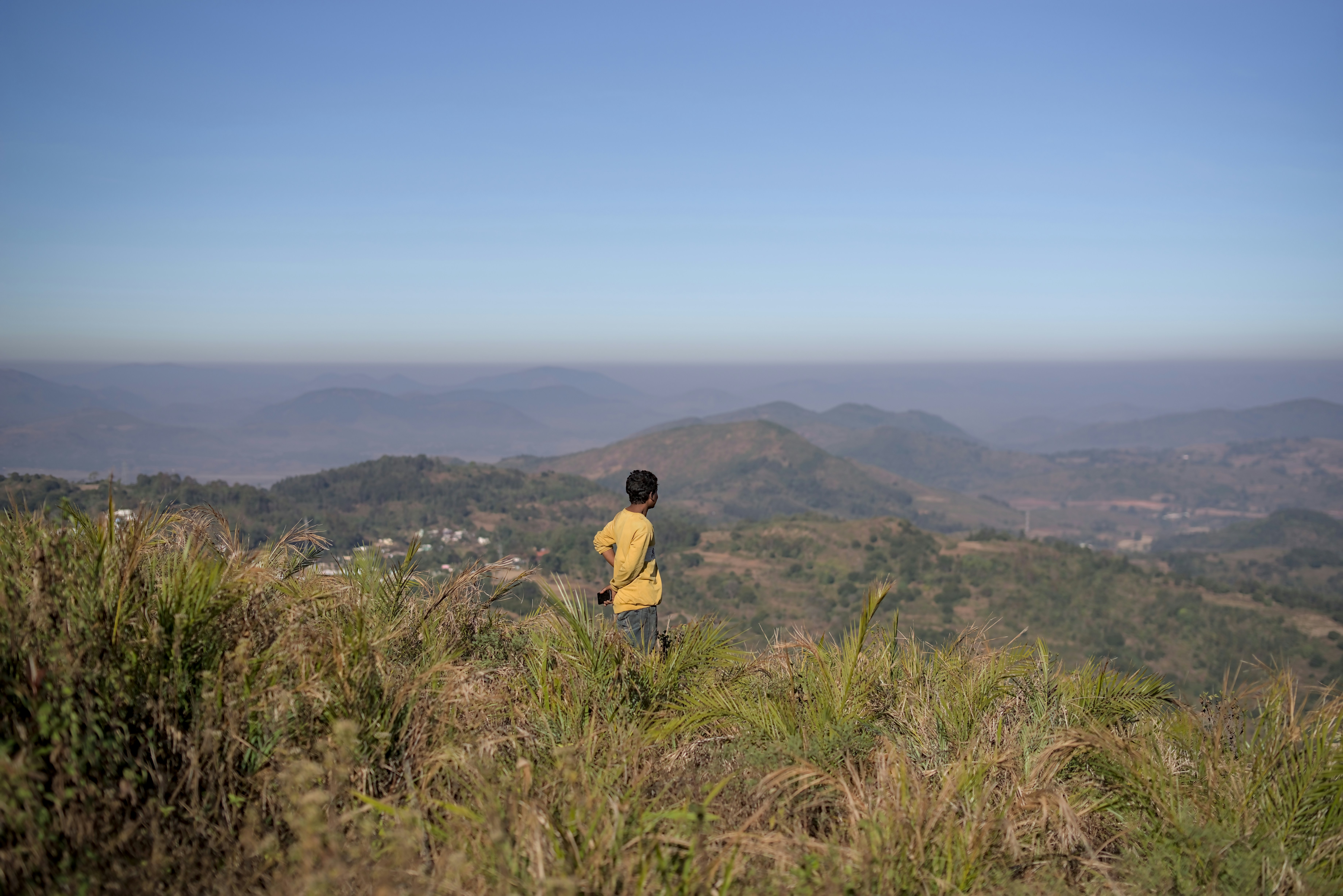 Man standing on grassy hilltop overlooking misty mountains