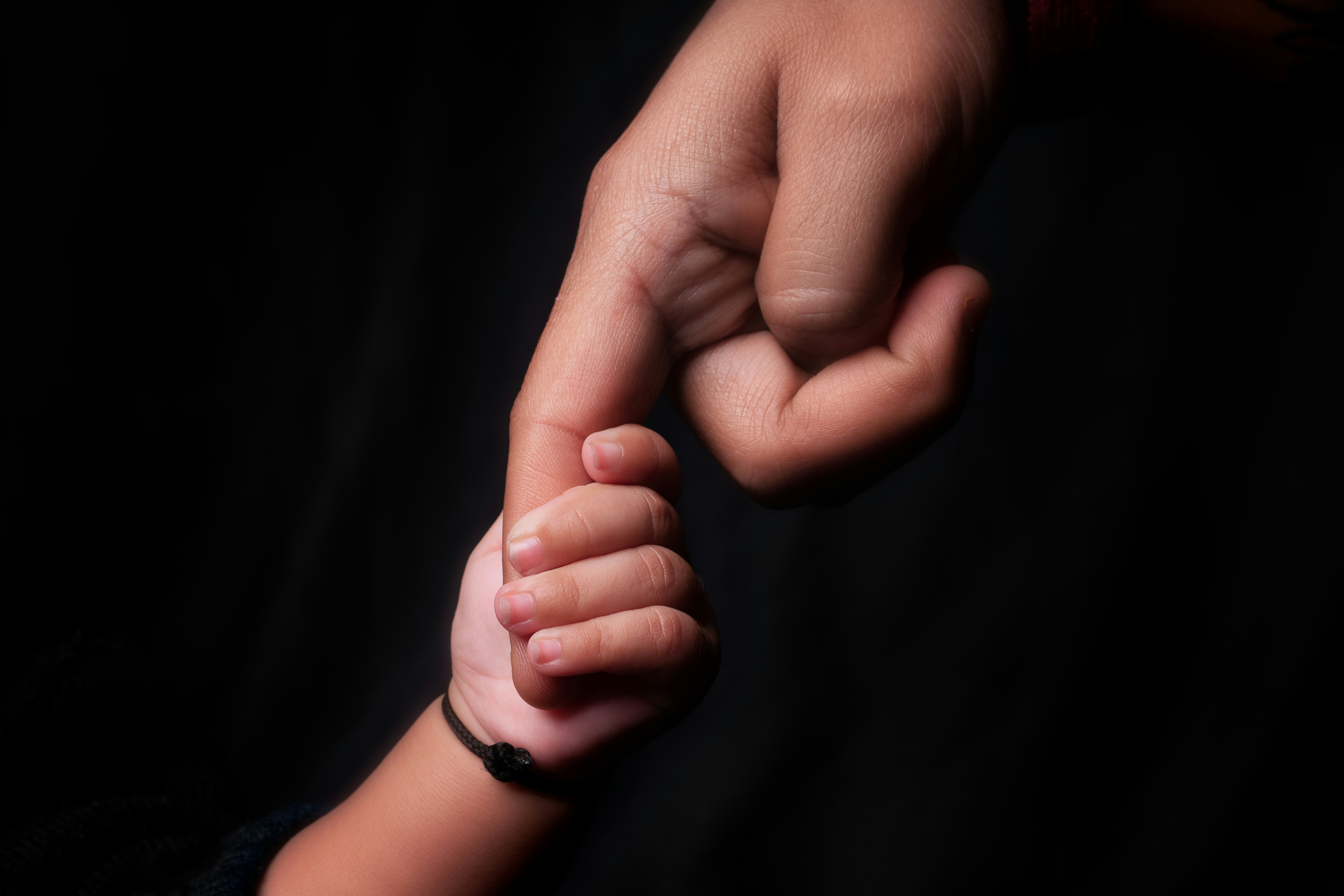 An adult holds a child's hand against a dark background