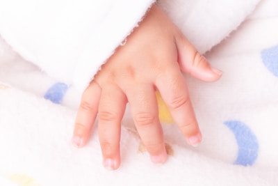 A baby's hand resting on a patterned blanket.