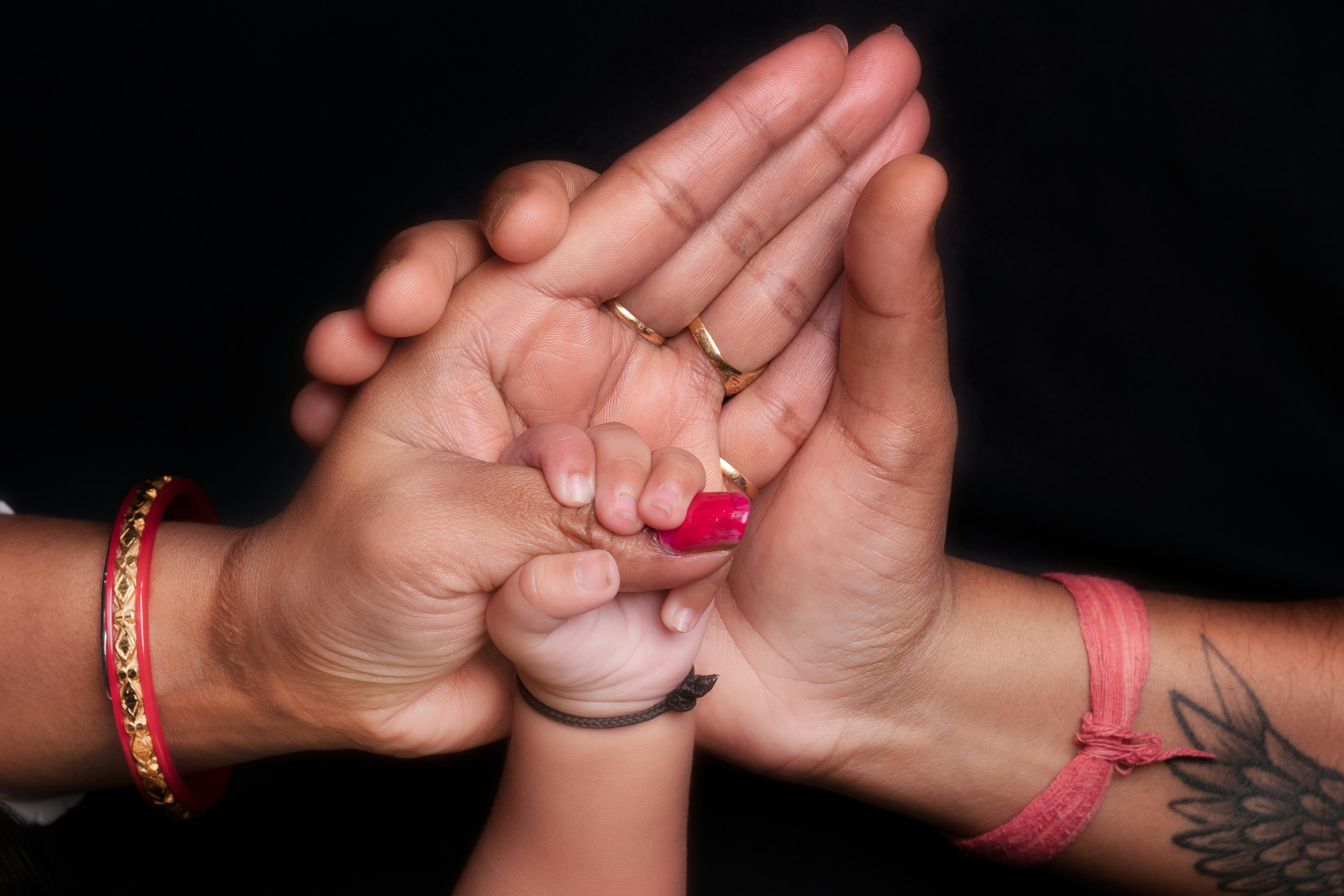 Drei Hände, zwei Erwachsene und ein Baby, ineinander verschränkt.