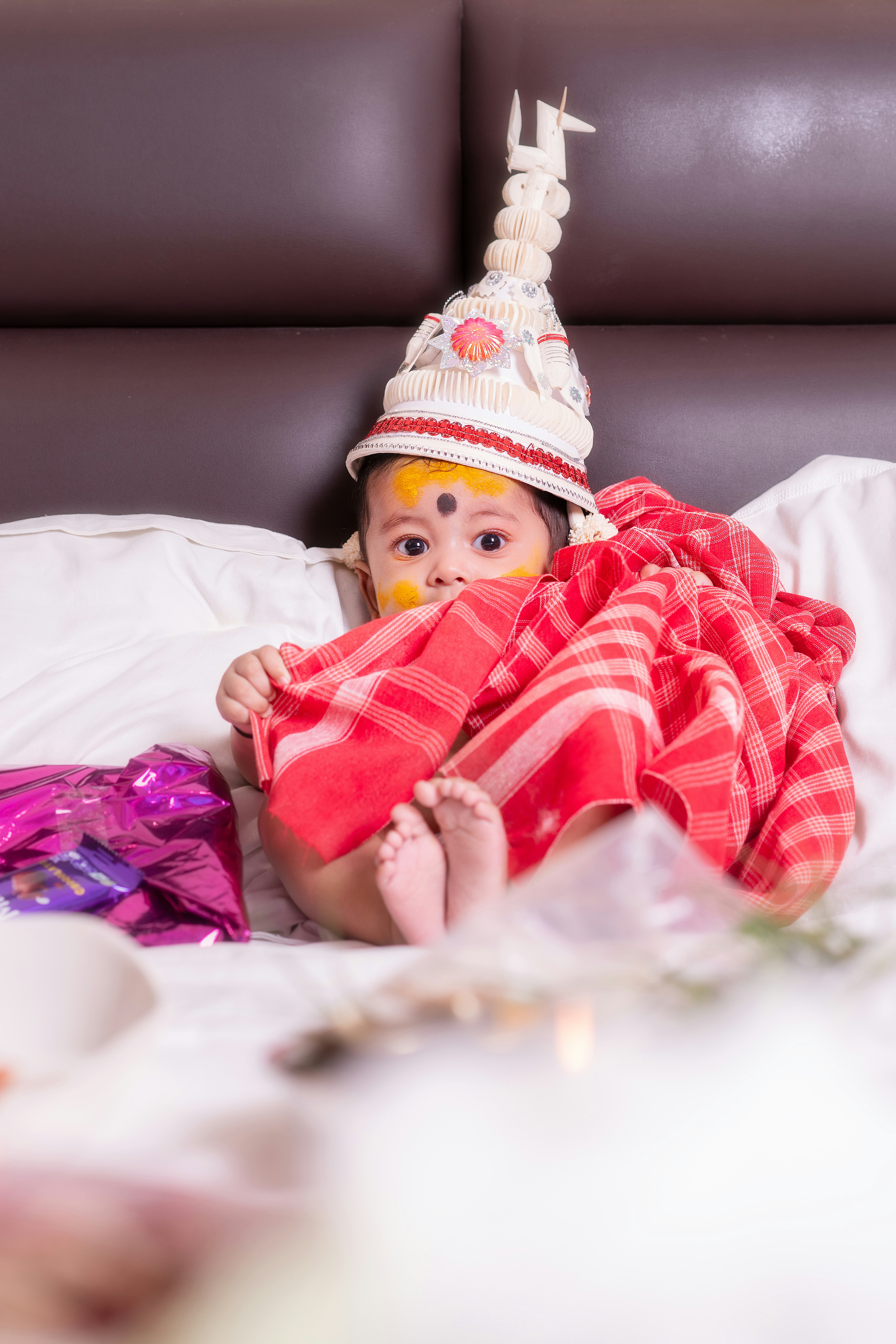 Seorang bayi yang mengenakan pakaian tradisional duduk di tempat tidur.