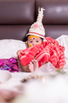 A baby dressed in traditional attire sits on a bed.
